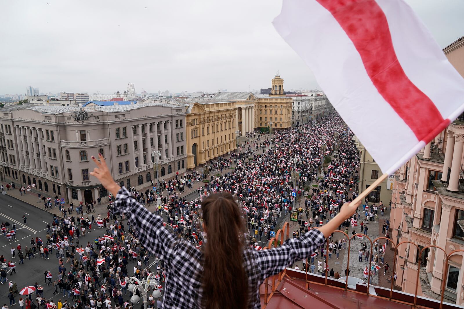 FILE - A woman waves an old Belarusian national flag from a roof as opposition supporters march to Independence Square in Minsk, Belarus, on Aug. 23, 2020. (AP Photo/Evgeniy Maloletka, File)