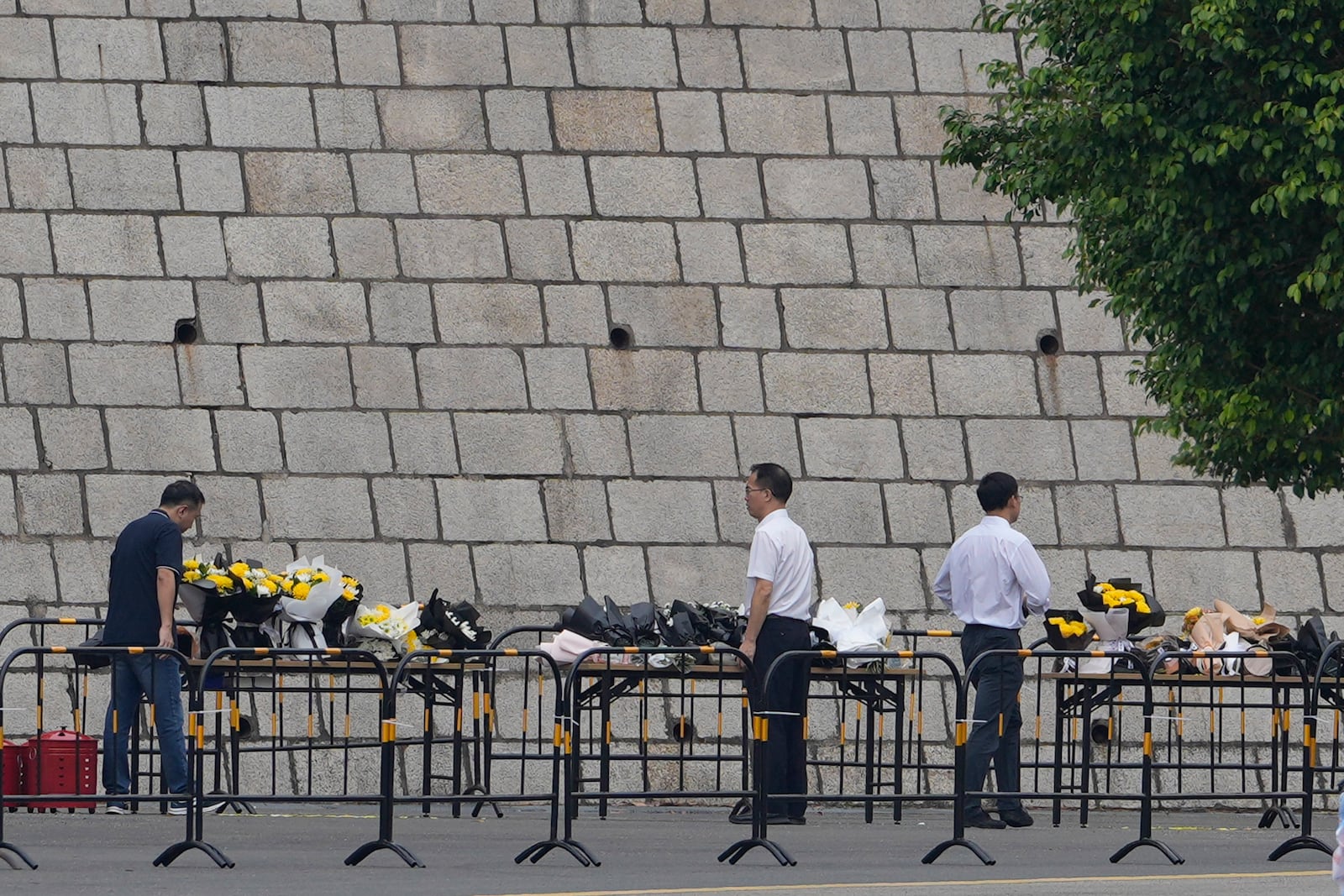 Volunteers relocate flowers laid outside "Zhuhai People's Fitness Plaza" to a barrier leading into the area where a man rammed his car into people exercising at the sports center, in Zhuhai in southern China's Guangdong province on Wednesday, Nov. 13, 2024. (AP Photo/Ng Han Guan)