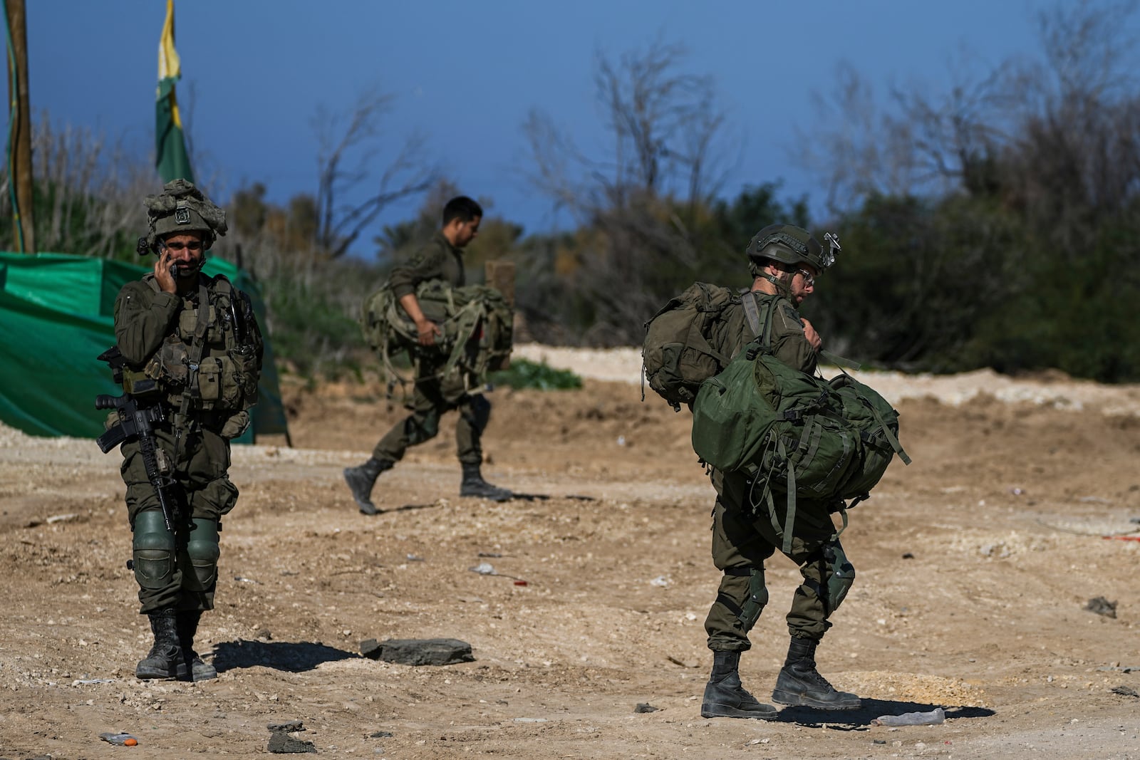 Israeli soldiers carry combat equipment as they return from the Gaza Strip at the Israeli-Gaza border, Saturday, Jan. 18, 2025. (AP Photo/Tsafrir Abayov)