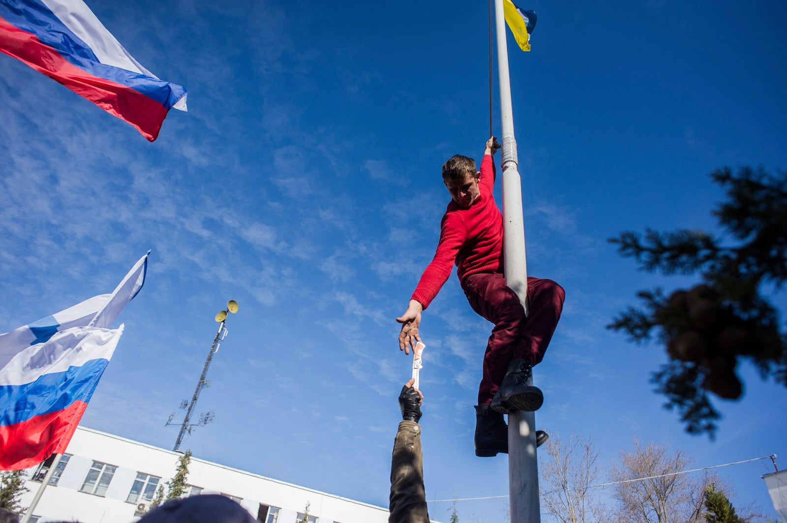 FILE - A member of a pro-Russian self-defense force reaches for a knife to take down a Ukrainian navy flag at the Ukrainian naval headquarters in Sevastopol, Crimea, March 19, 2014. (AP Photo, File)