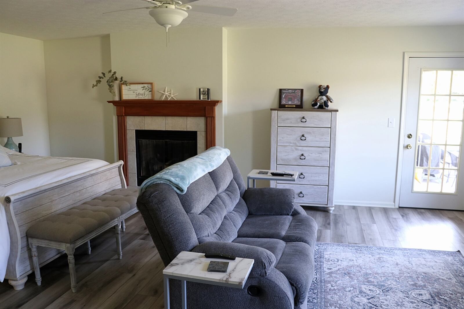 The dual-sided gas fireplace is nestled within the primary bedroom and has a raised ceramic-tile hearth and wood beam mantel. A glass-panel door opens from the bedroom to the covered rear porch; and two windows look out over the deep, semi-private backyard.