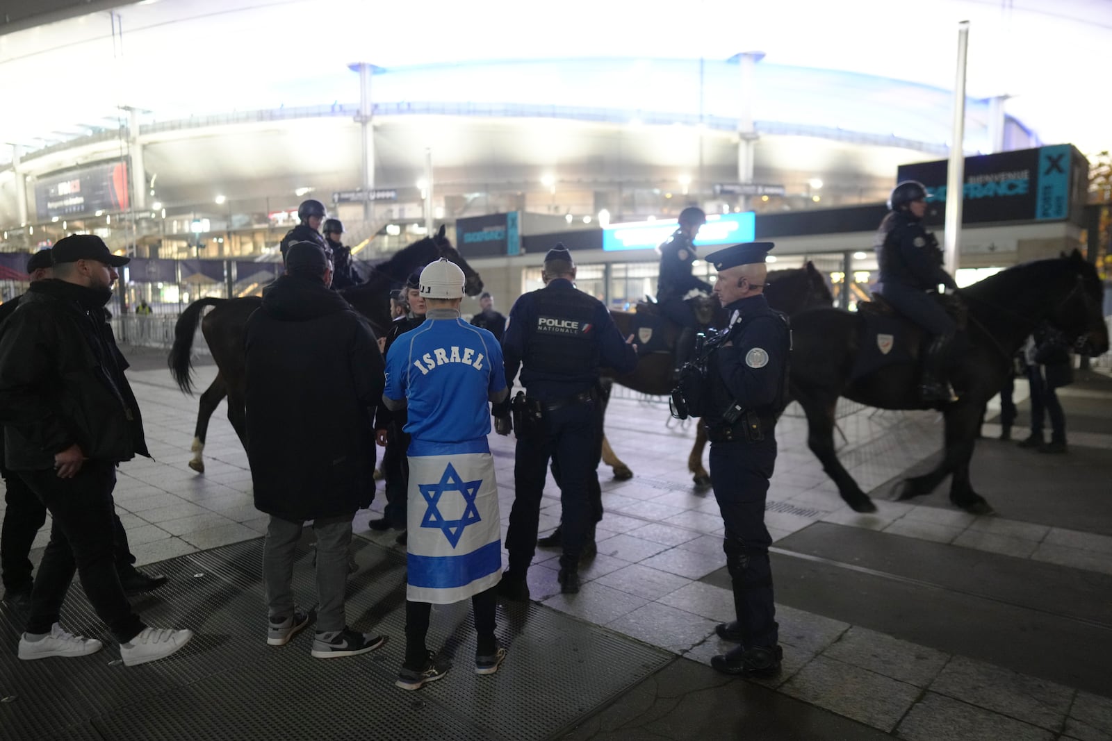 Police check a man covered with an Israeli flag next to the Stade de France before the UEFA Nations League soccer match between France and Israel, in Saint-Denis, outside Paris, Thursday, Nov. 14, 2024. (AP Photo/Thibault Camus)