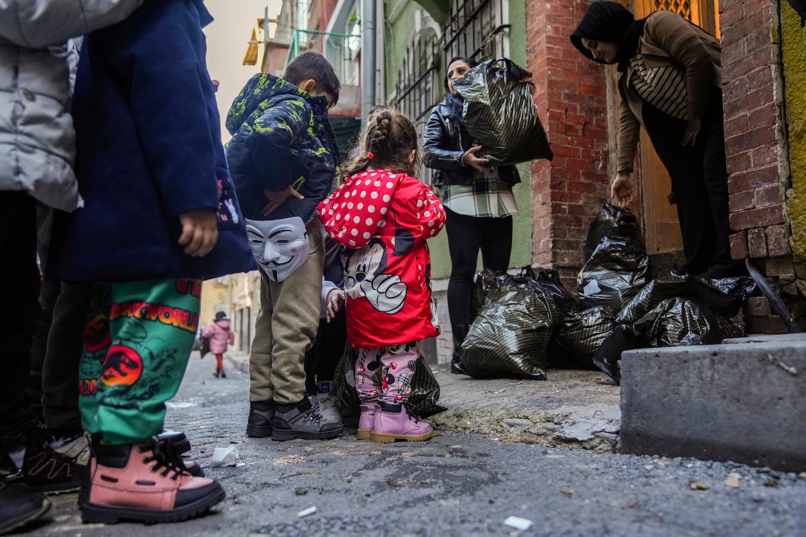 Children and their families wait their turn as coats and shoes are handed out by volunteers in the Tarlabasi neighborhood in Istanbul, Turkey, Saturday, Dec. 14, 2024. (AP Photo/Francisco Seco)