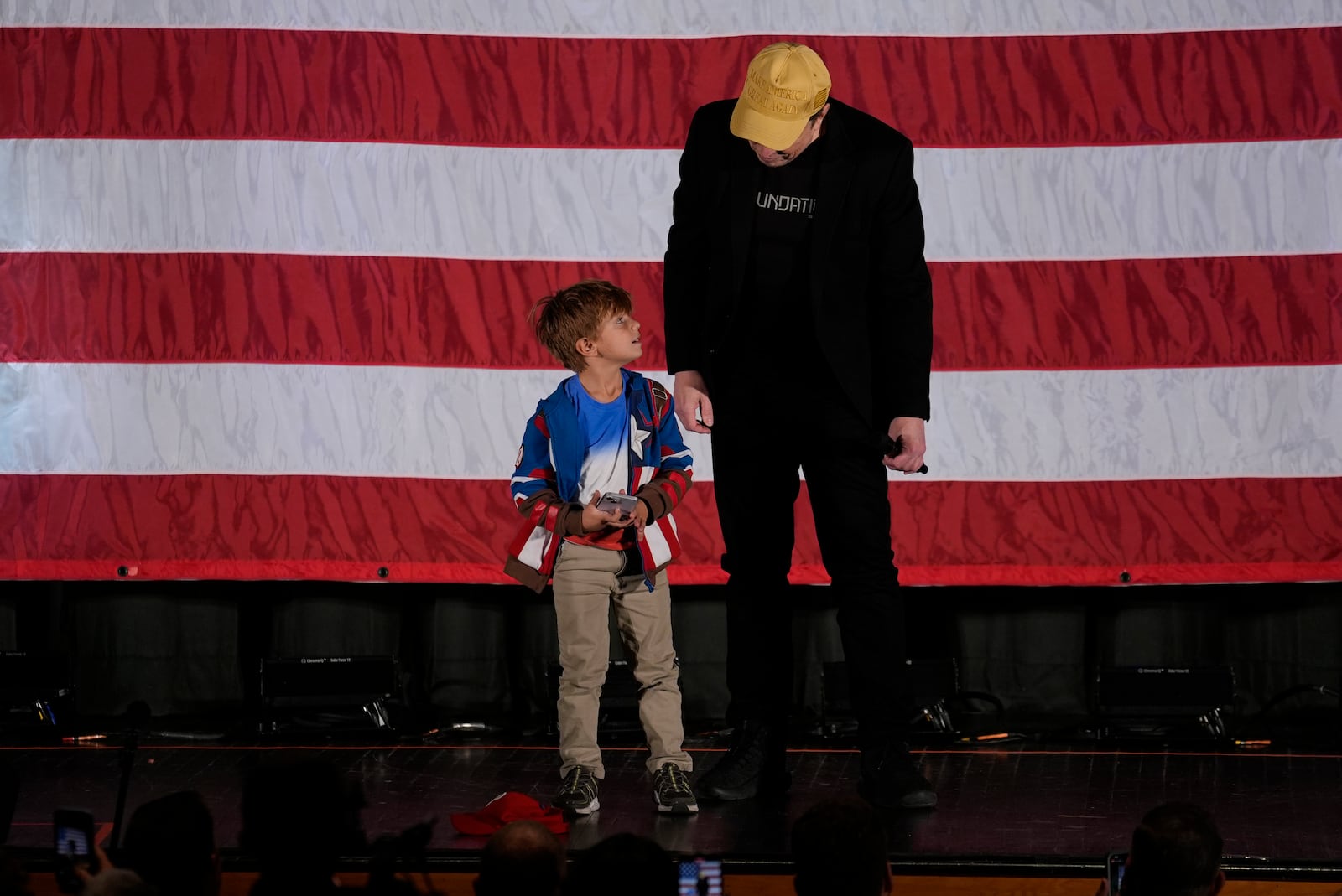 Elon Musk talks with a child as he speaks as part of a campaign town hall in support of Republican presidential nominee former President Donald Trump in Folsom, Pa., Thursday, Oct. 17, 2024. (AP Photo/Matt Rourke)