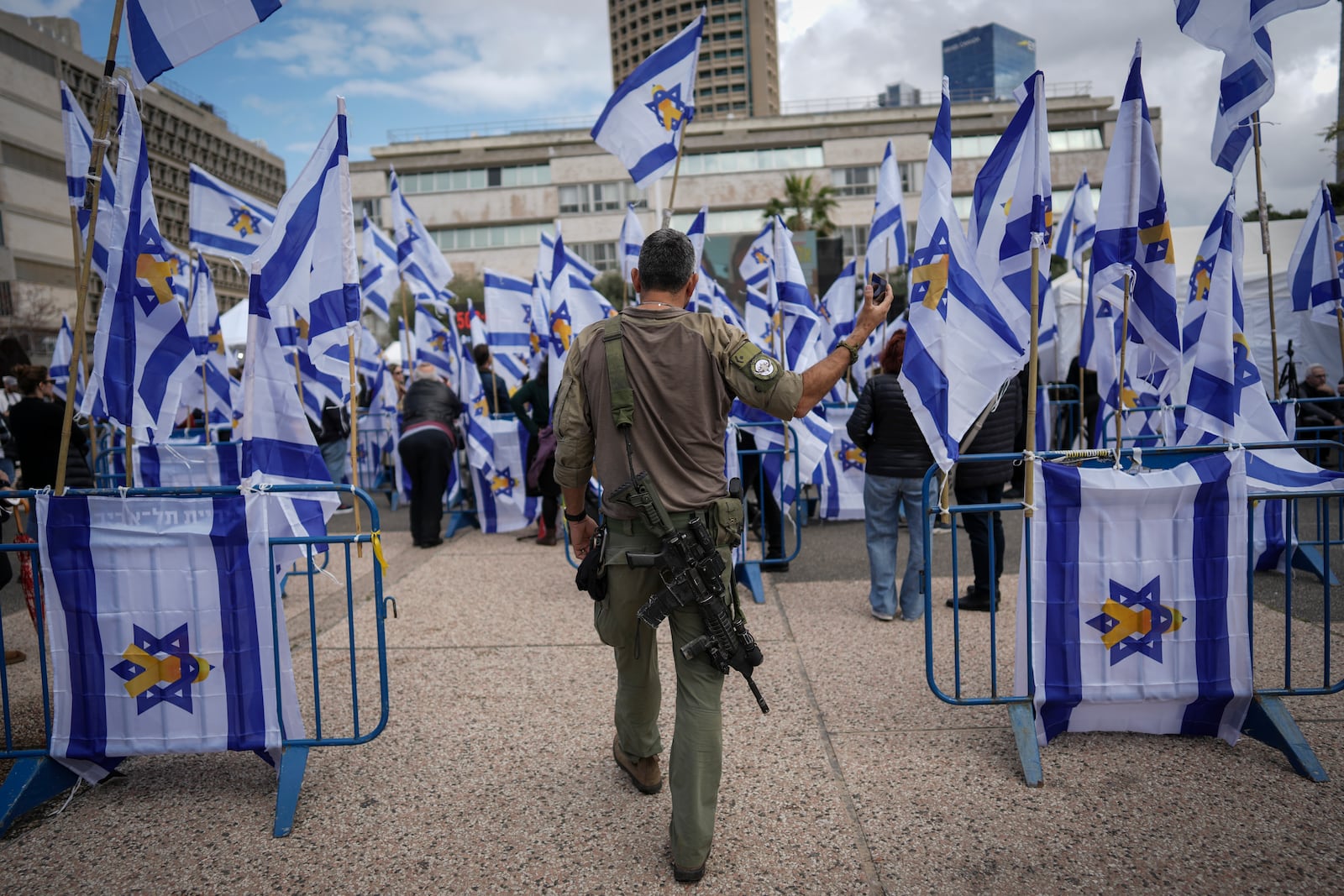 An Israeli soldier holds his cellphone as he walks into "Hostages Square" in Tel Aviv, Israel, Thursday, Feb. 20, 2025, as Palestinian militant groups hand over the bodies of four Israeli hostages, including a mother and her two children, to the Red Cross in Gaza.(AP Photo/Oded Balilty)