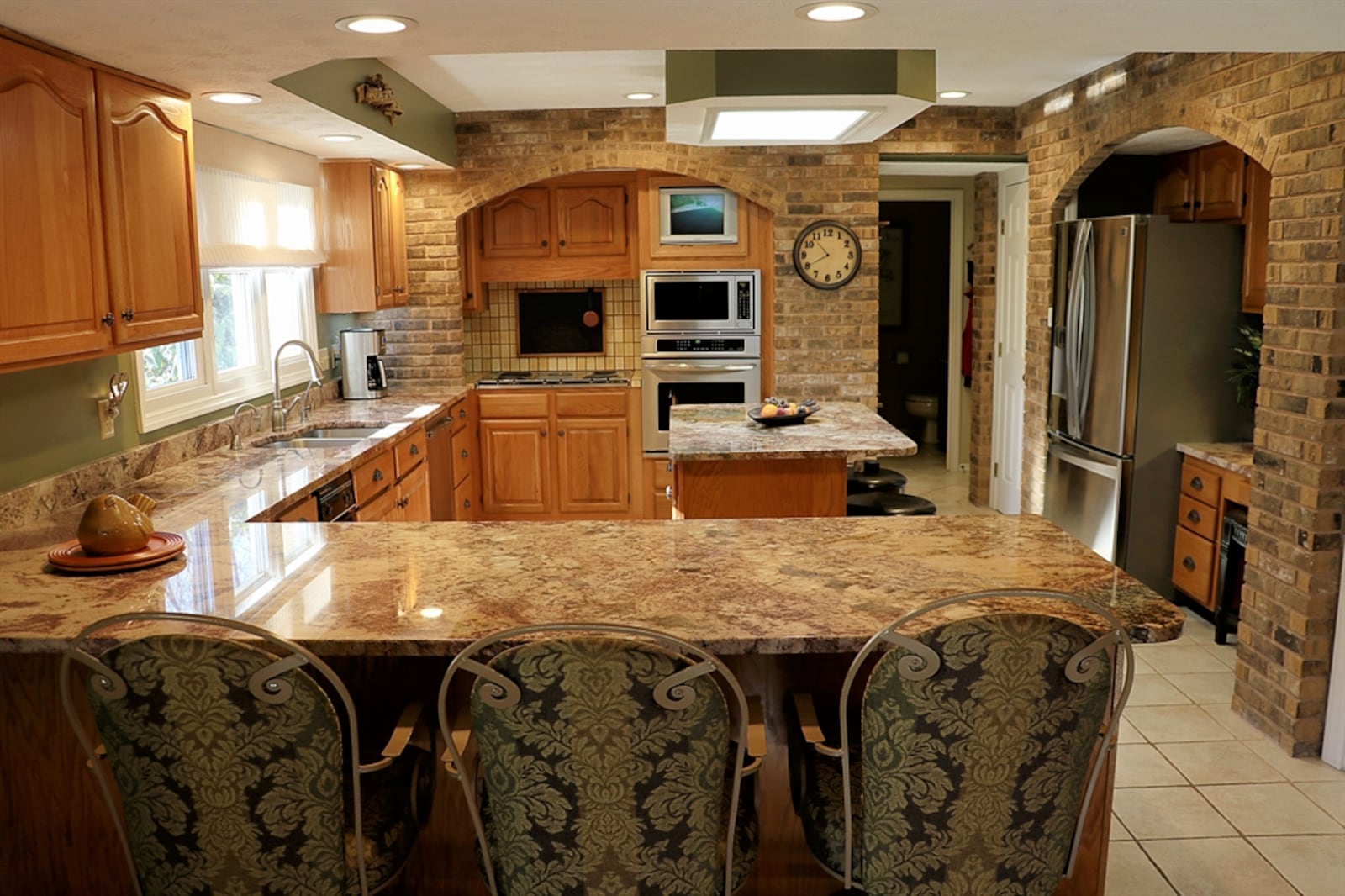 The kitchen has brick wall accents with appliance and counter space nooks. A window is above the sink and an island offers seating and storage. Granite counters allow for a planning area and coffee station.