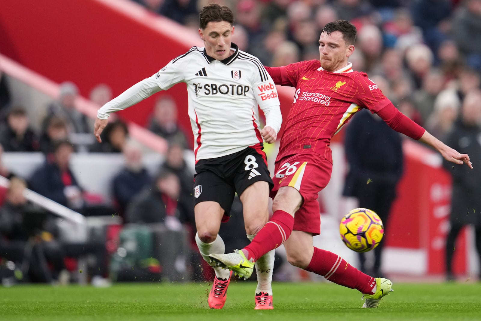 Liverpool's Andrew Robertson, right, duels for the ball with Fulham's Harry Wilson during the English Premier League soccer match between Liverpool and Fulham, at Anfield stadium in Liverpool, England, Saturday, Dec. 14, 2024. (AP Photo/Jon Super)