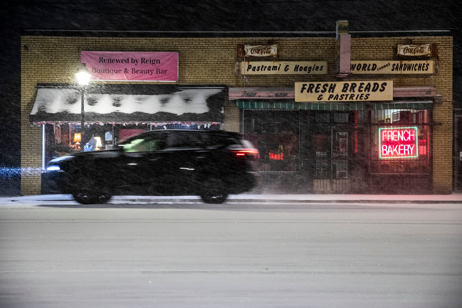 A vehicle travels along a snow-covered Granby Street in the Riverview Village area of Norfolk, Va. on Tuesday, Jan. 21, 2025. (Kendall Warner / The Virginian-Pilot via AP)