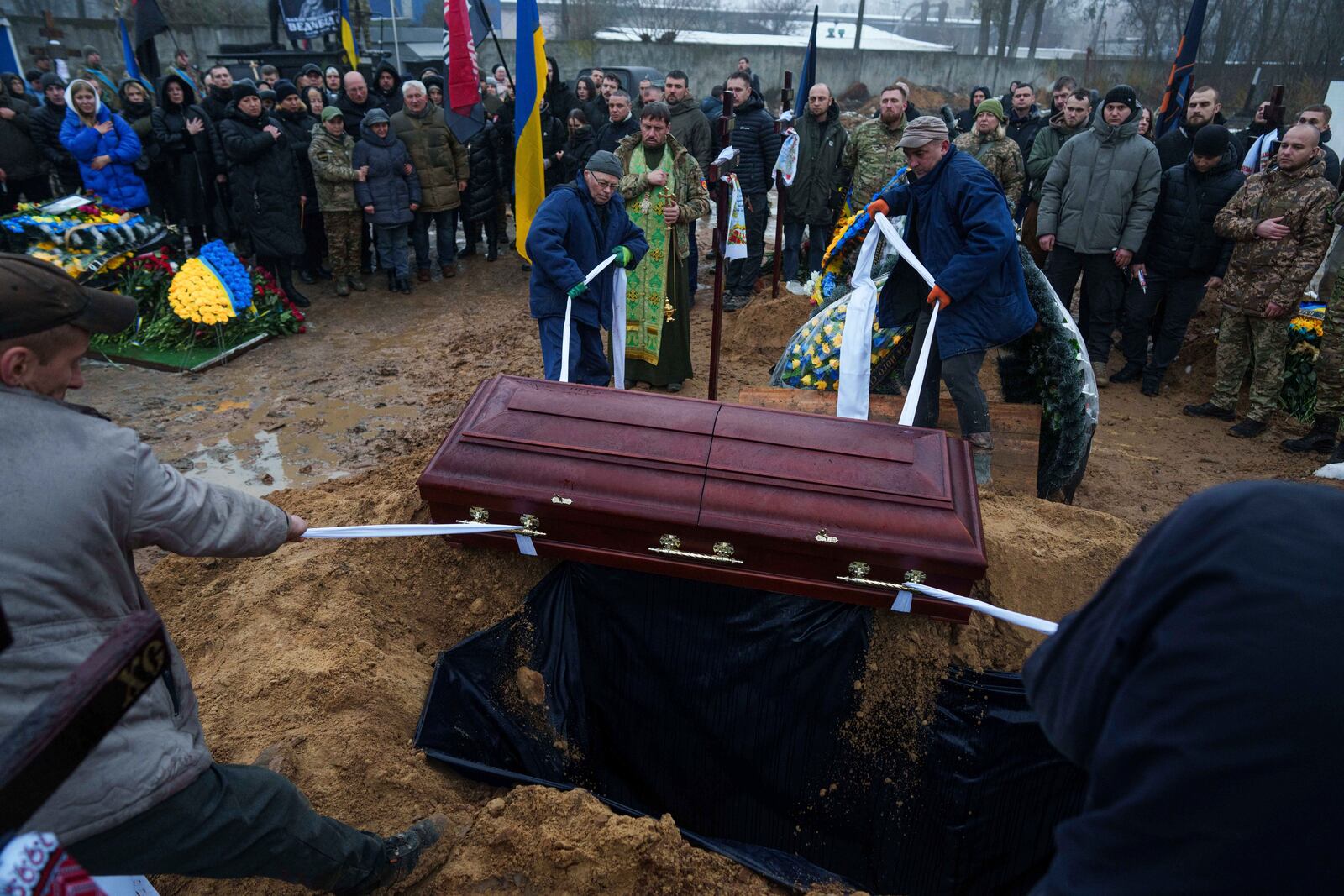 Funeral workers down a coffin into grave during the funeral ceremony of a Ukrainian officer Pavlo Vedybida aka "Obolonchik" in a cemetery in Kyiv, Ukraine, Saturday, Nov. 30, 2024. (AP Photo/Evgeniy Maloletka)