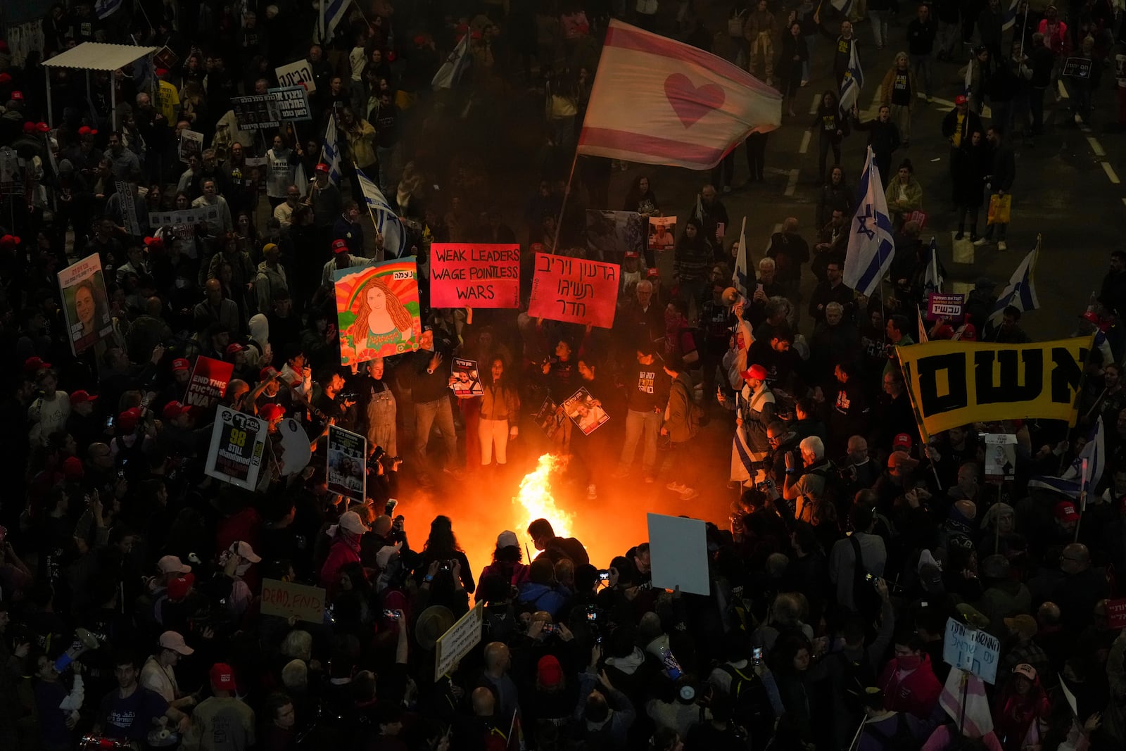 Demonstrators light a bonfire during a protest demanding a cease-fire deal and the immediate release of hostages held by Hamas, in Tel Aviv, Israel, Saturday, Jan. 11, 2025. (AP Photo/Ariel Schalit)