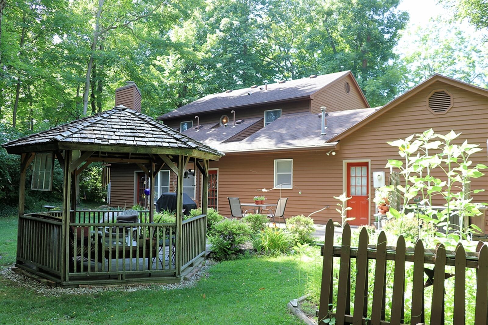 Lush landscaping surrounds a backyard gazebo, fire pit with seating and concrete patio with picket-fence accents.