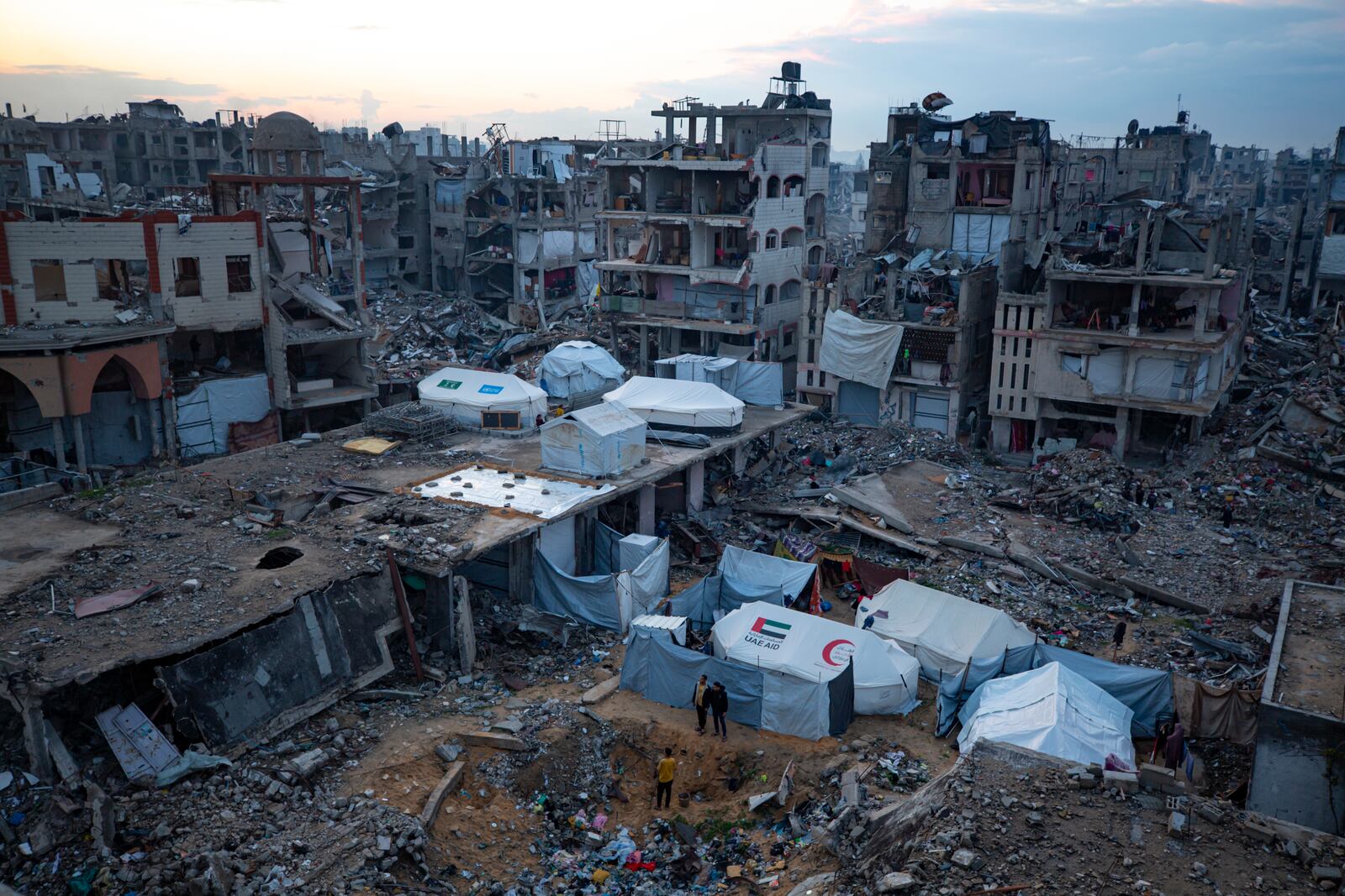 Palestinians stand next to tents surrounded by buildings that were destroyed by the Israeli air and ground offensive in Jabaliya, Gaza Strip, Tuesday, Feb. 11, 2025. (AP Photo/Jehad Alshrafi)