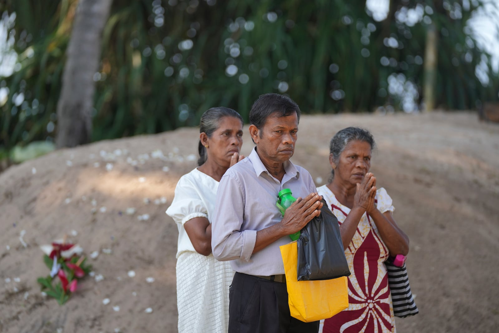 Relatives pray for their dead relatives in 2004 Indian Ocean tsunami, standing by a mass grave during a memorial of the 20th anniversary of the calamity in Peraliya, Sri Lanka, Thursday, Dec. 26, 2024. (AP Photo/Eranga Jayawardena)