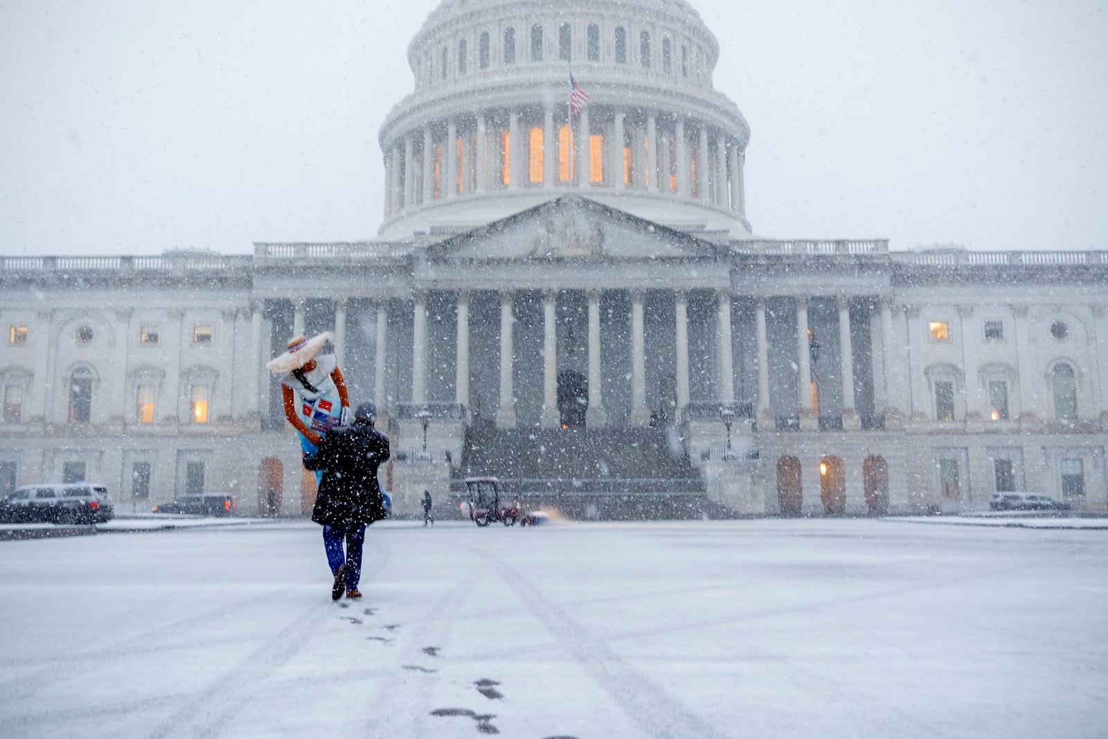 A man carries a mannequin wearing an outfit featuring an American and Dominican Republic flag as snow falls, at the Capitol, Tuesday, Feb. 11, 2025, during a snowstorm in Washington. (AP Photo/Jacquelyn Martin)