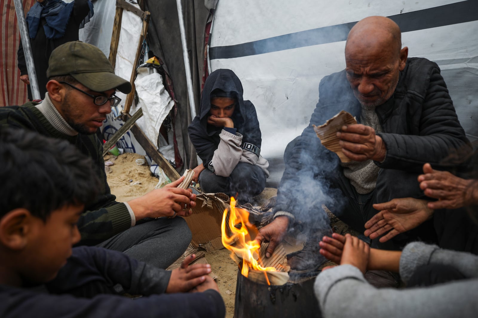 Members of Abed family, warm up by a fire at a tent camp for displaced Palestinians at the Muwasi, Rafah, southern Gaza Strip, Monday, Feb. 24, 2025. (AP Photo/Jehad Alshrafi)