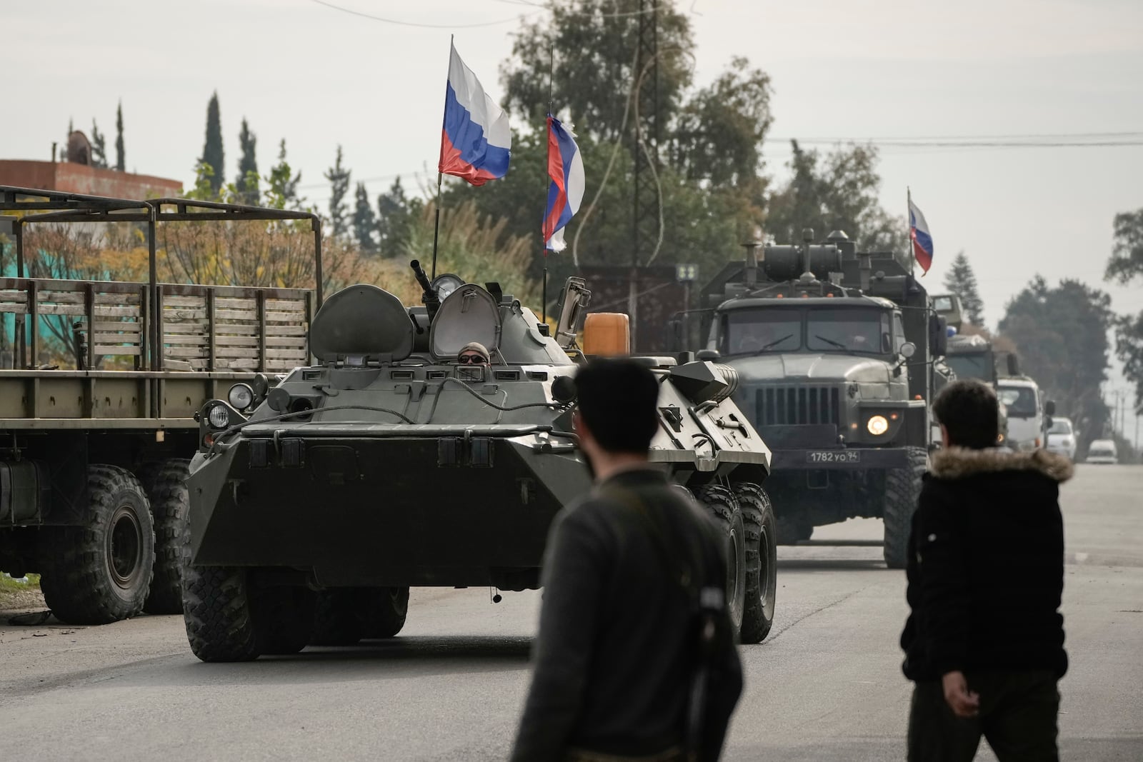 Syrian fighters watch Russian armoured vehicles driving past near the Hmeimim Air Base, a Syrian airbase currently operated by Russia, in the town of Hmeimim, southeast of Latakia, Syria, Monday Dec. 16, 2024.(AP Photo/Leo Correa)