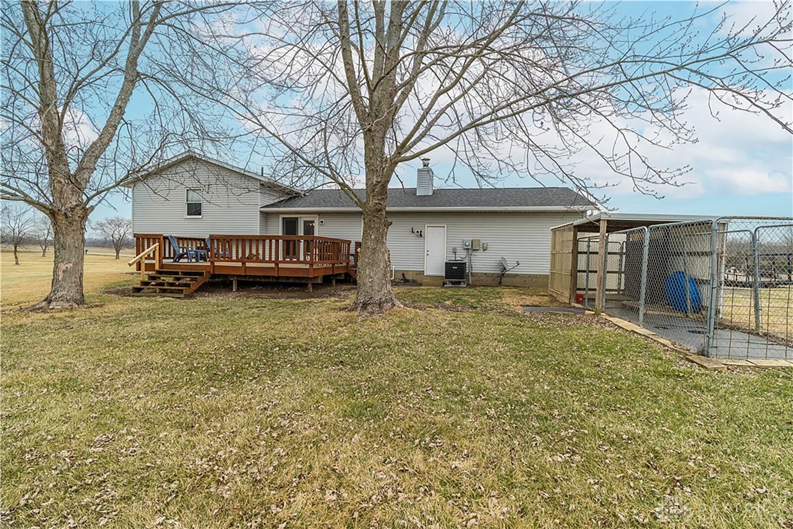 The rear of the property features a wood deck with railings and a fenced kennel area.