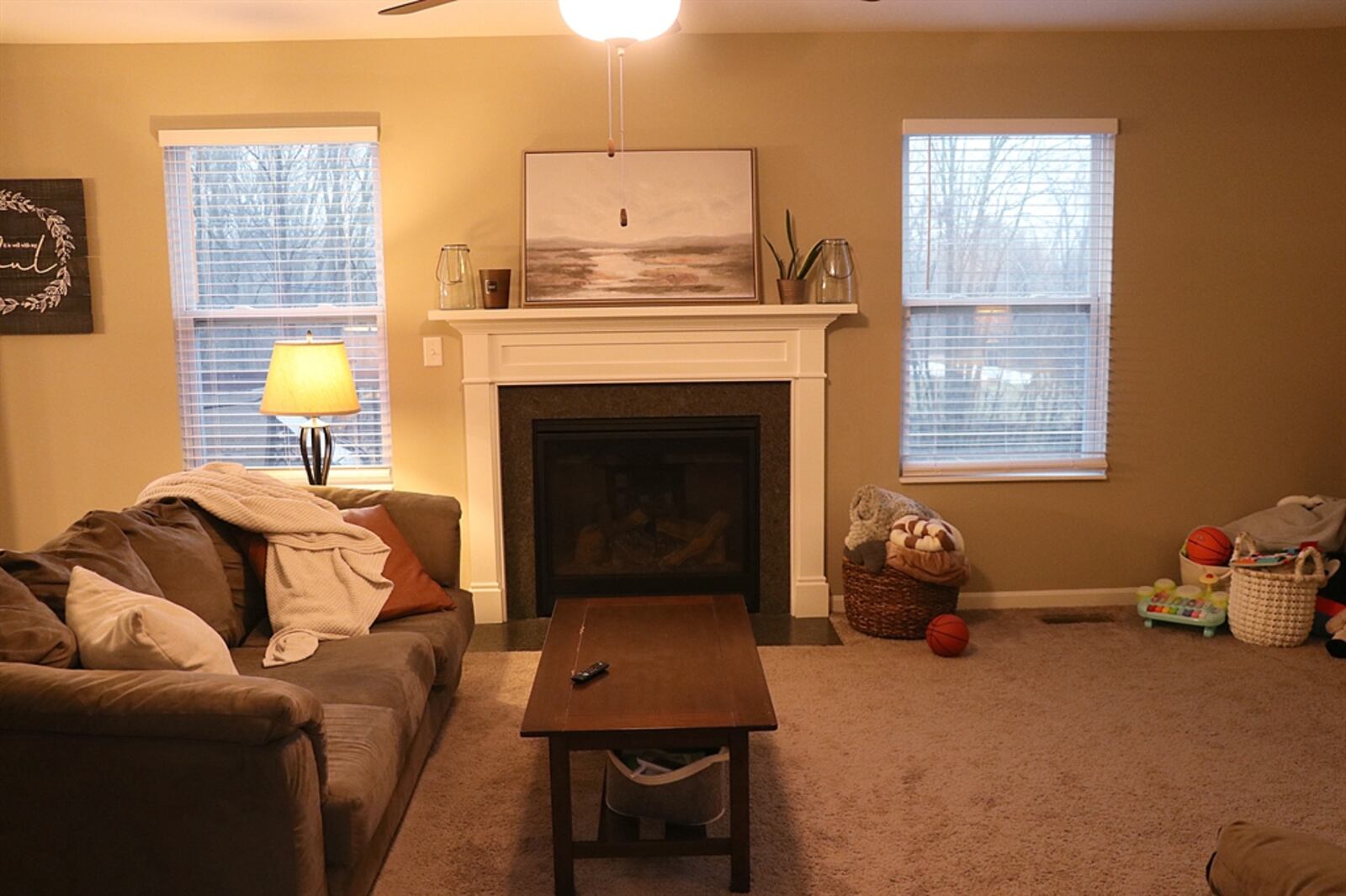 A gas fireplace with fluted wood mantel and marble hearth is flanked by two windows and is the centerpiece to the great room.