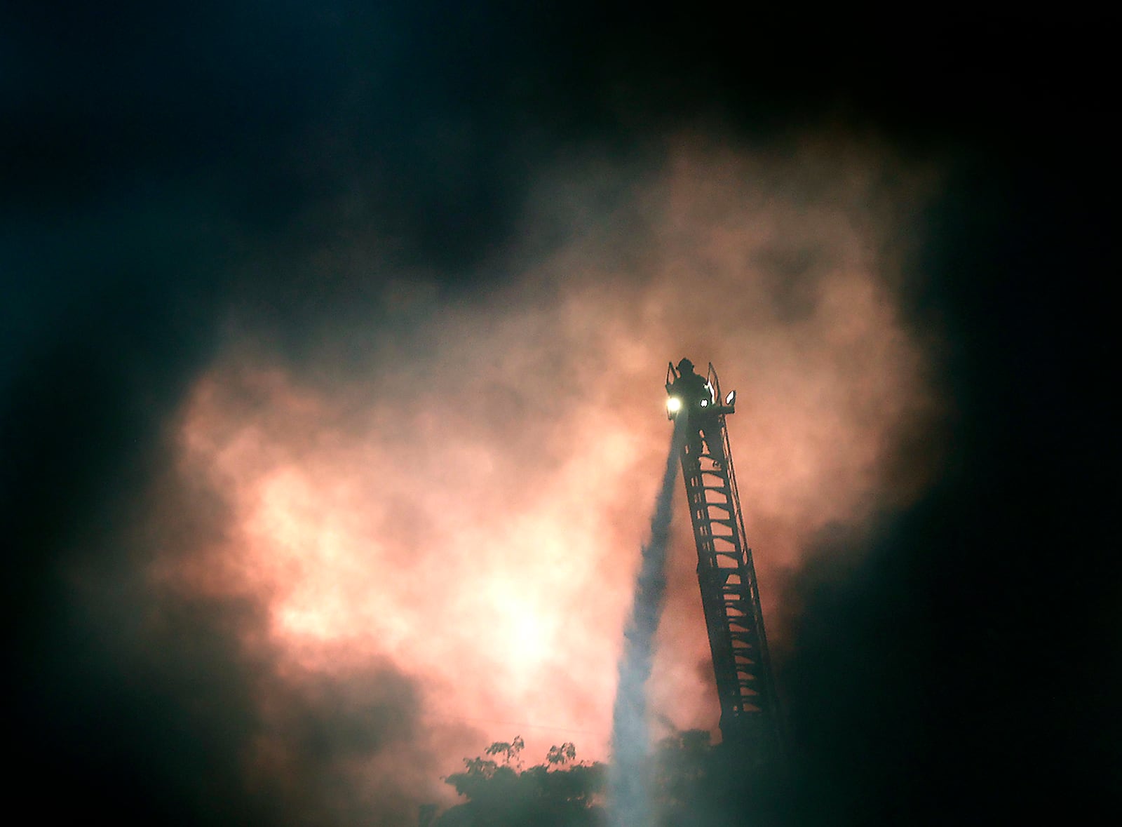 The smoke from an industrial fire at USA Trucking on Leffel Lane parts long enough to reveal a member of the Springfield Fire Division, on top of an aerial truck ladder, spraying water on the fire Friday, June 2, 2023.