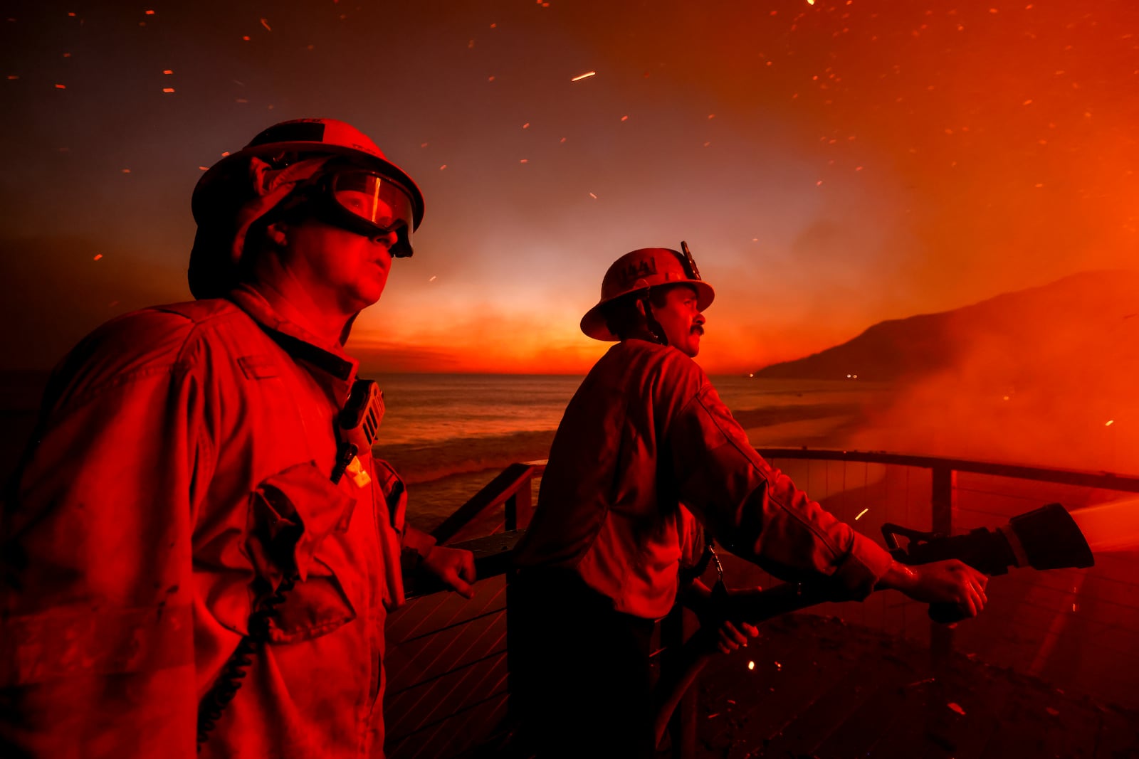 Firefighters work from a deck as the Palisades Fire burns a beachfront property Wednesday, Jan. 8, 2025 in Malibu, Calif. (AP Photo/Etienne Laurent)