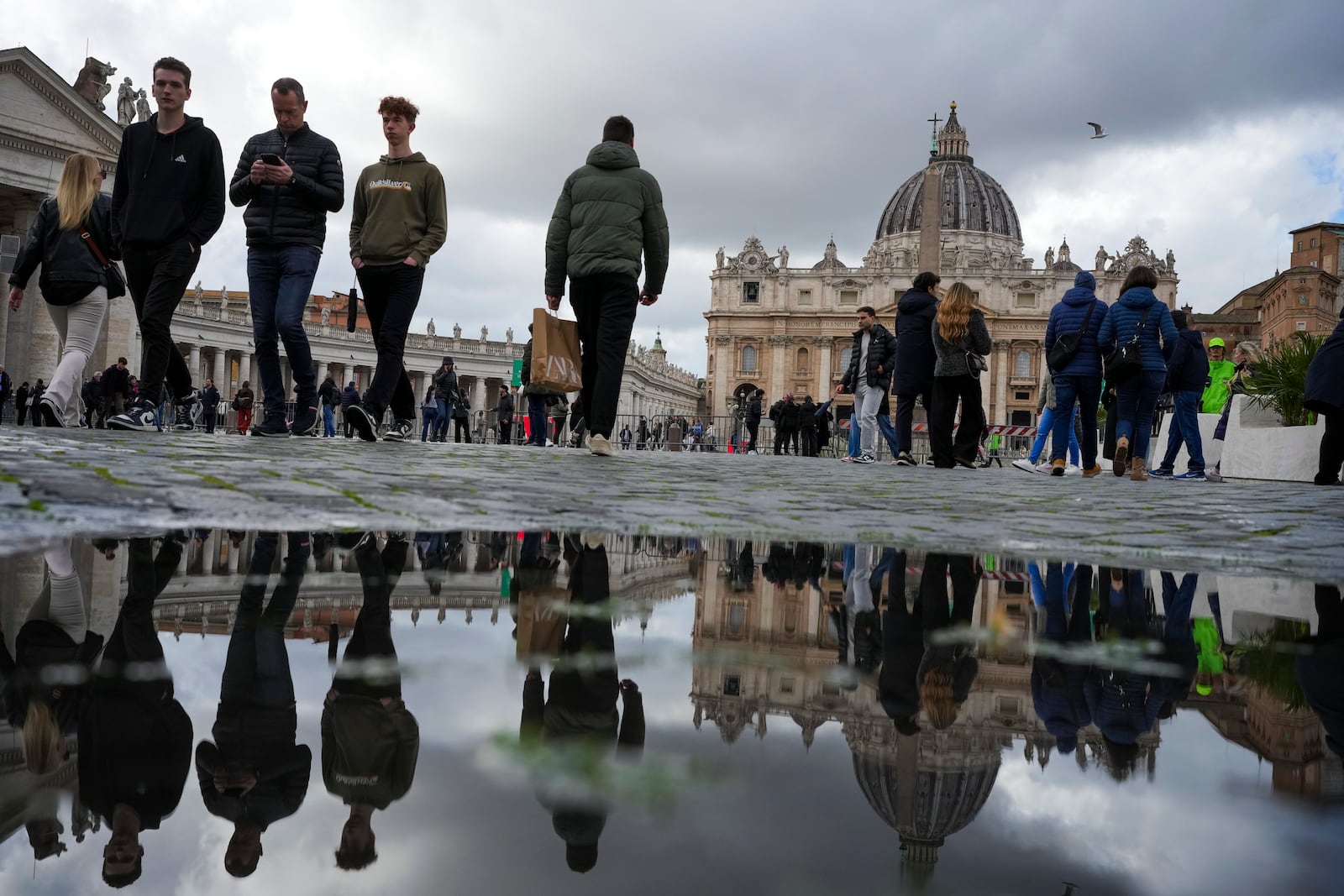 People walk in St. Peter's Square at The Vatican, Friday, Feb. 14, 2025, hours after Pope Francis was hospitalized to undergo some necessary diagnostic tests and to continue his ongoing treatment for bronchitis. (AP Photo/Alessandra Tarantino)