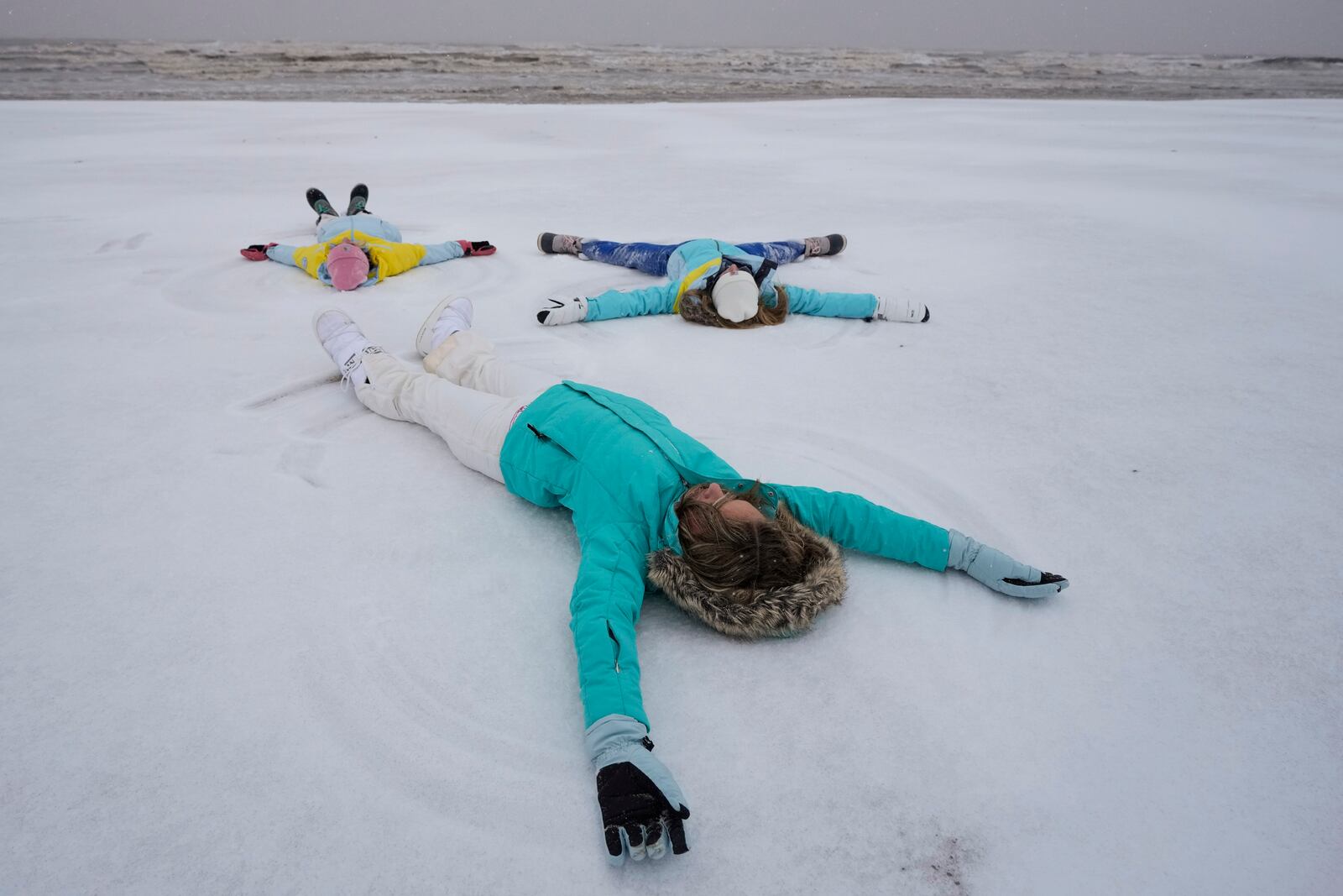 Madison Gaido, and her sisters, Ellie and Kate make snow angels on the beach during an icy winter storm on Tuesday, Jan. 21, 2025 in Galveston, Texas. (Brett Coomer/Houston Chronicle via AP)