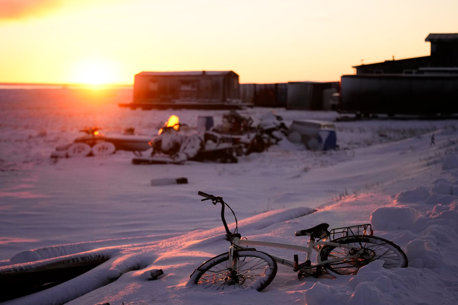 The sun rises over a bicycle covered in snow at the edge of the village in Kaktovik, Alaska, Tuesday, Oct. 15, 2024. (AP Photo/Lindsey Wasson)