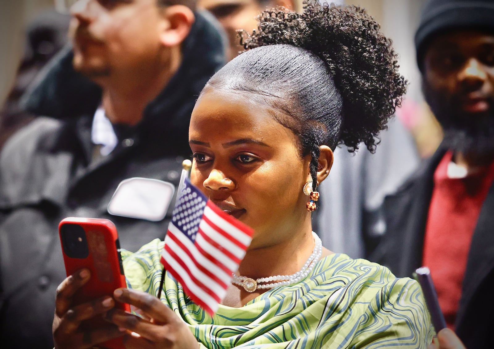 A girl holds an American flag as she records a naturalization ceremony on her cellphone Thursday, Jan. 23, 2025, at Oakwood High School School. Thirty-eight people from 22 different countries became U.S. citizens. MARSHALL GORBY\STAFF