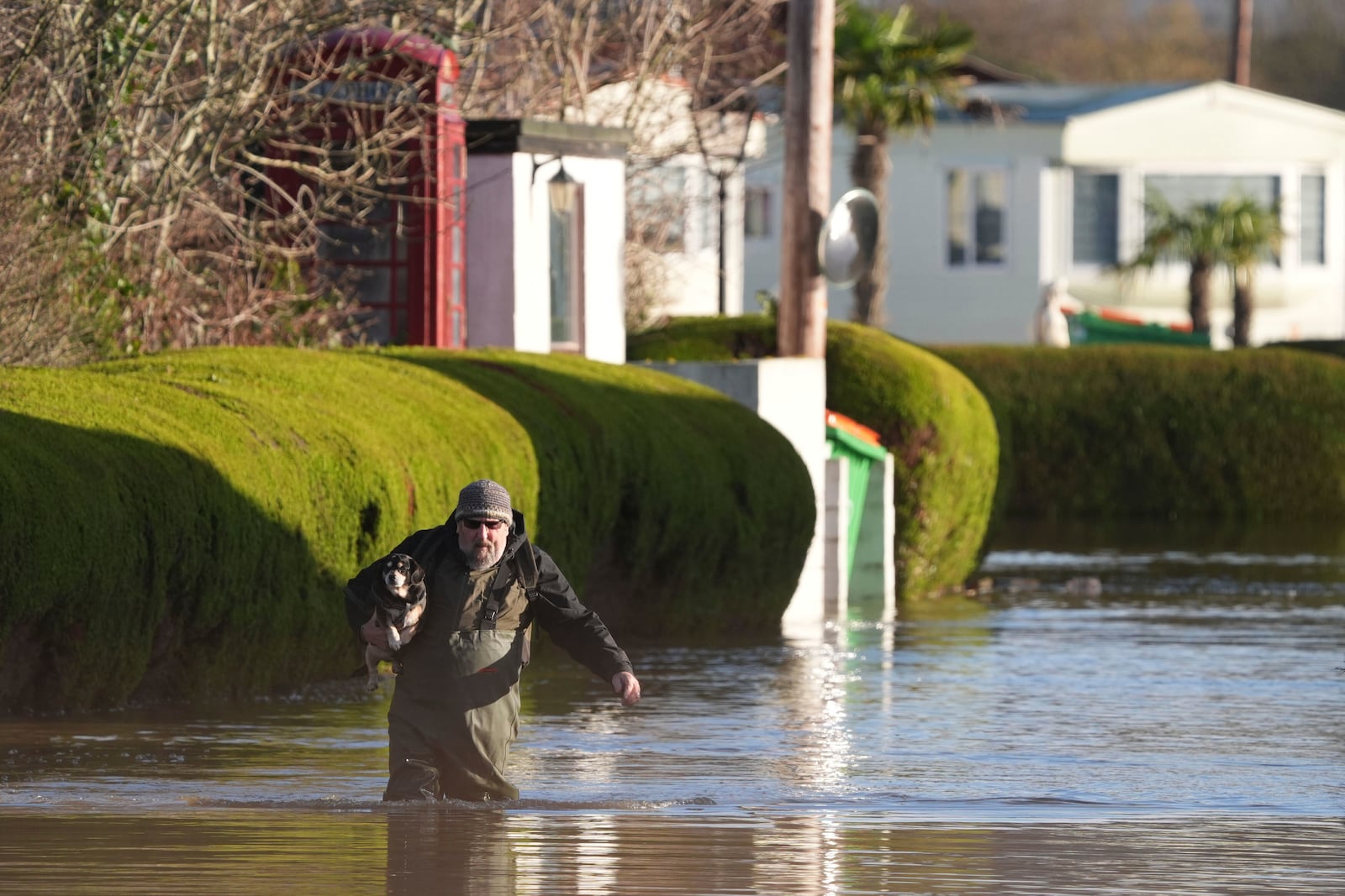 A man wearing waders carries a dog at The Little Venice caravan park, surrounded by rising flood water, in Yalding, England, Tuesday, Jan. 7, 2025, as weather warnings were issued across much of the UK. (Gareth Fuller/PA via AP)