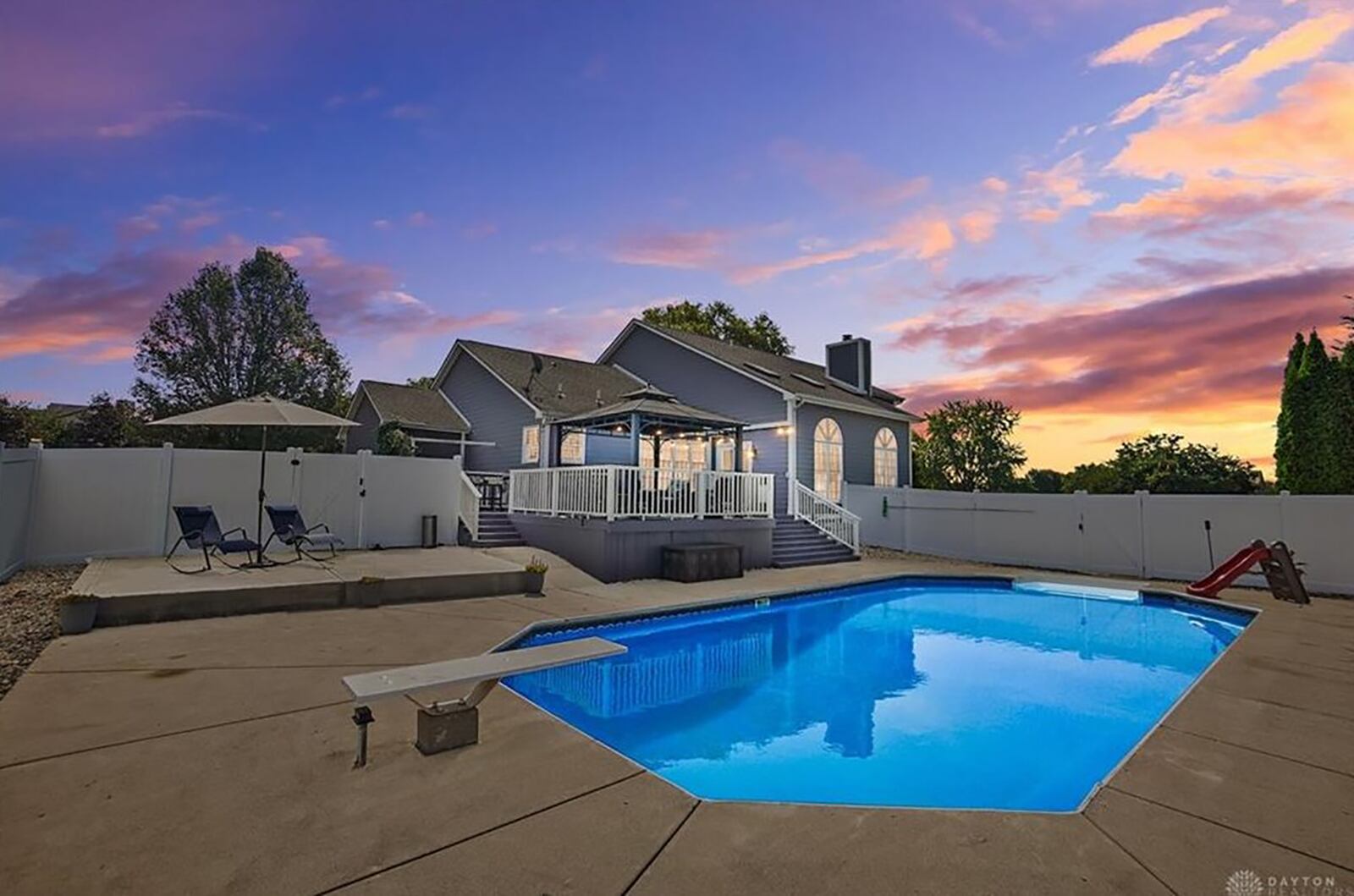 The backyard inground pool is surrounded by an extended concrete deck and vinyl privacy fence. There is also a raised patio and diving board.