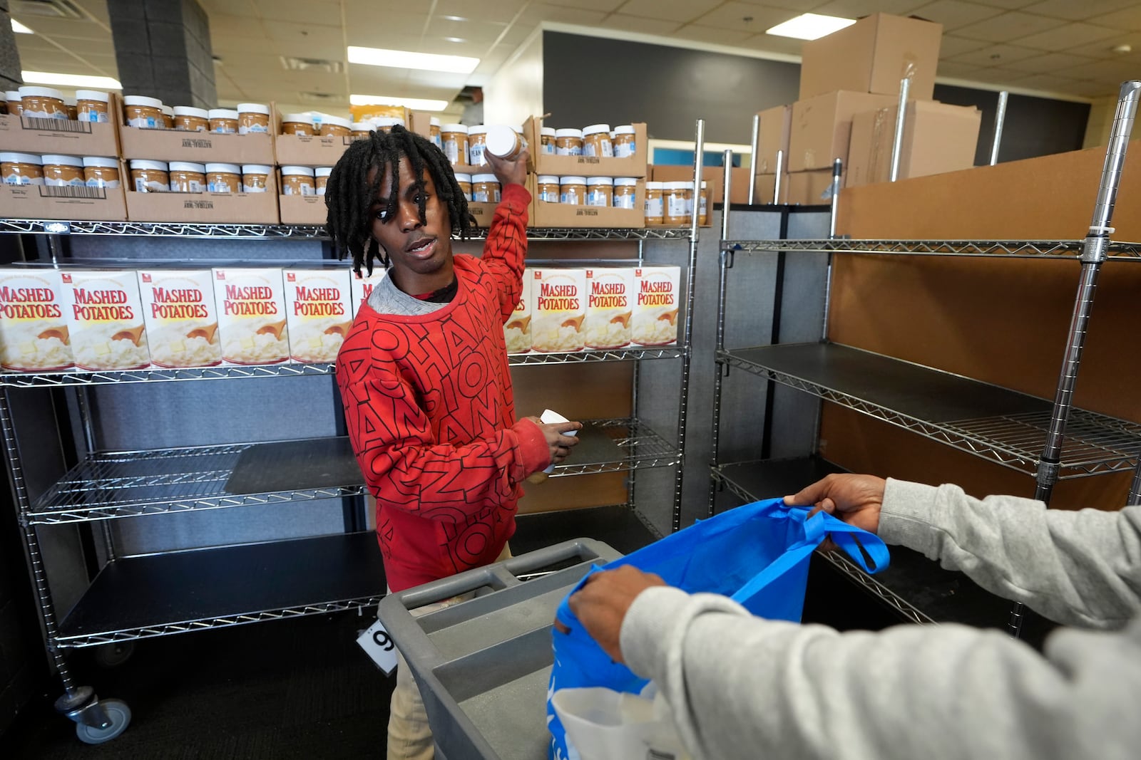 Volunteer Jaylund Asare, of Providence, R.I., center, assists Hungria Hernandez Diomedes, hands only at right, in a food pantry at Federal Hill House, Tuesday, Nov. 12, 2024, in Providence, R.I. (AP Photo/Steven Senne)