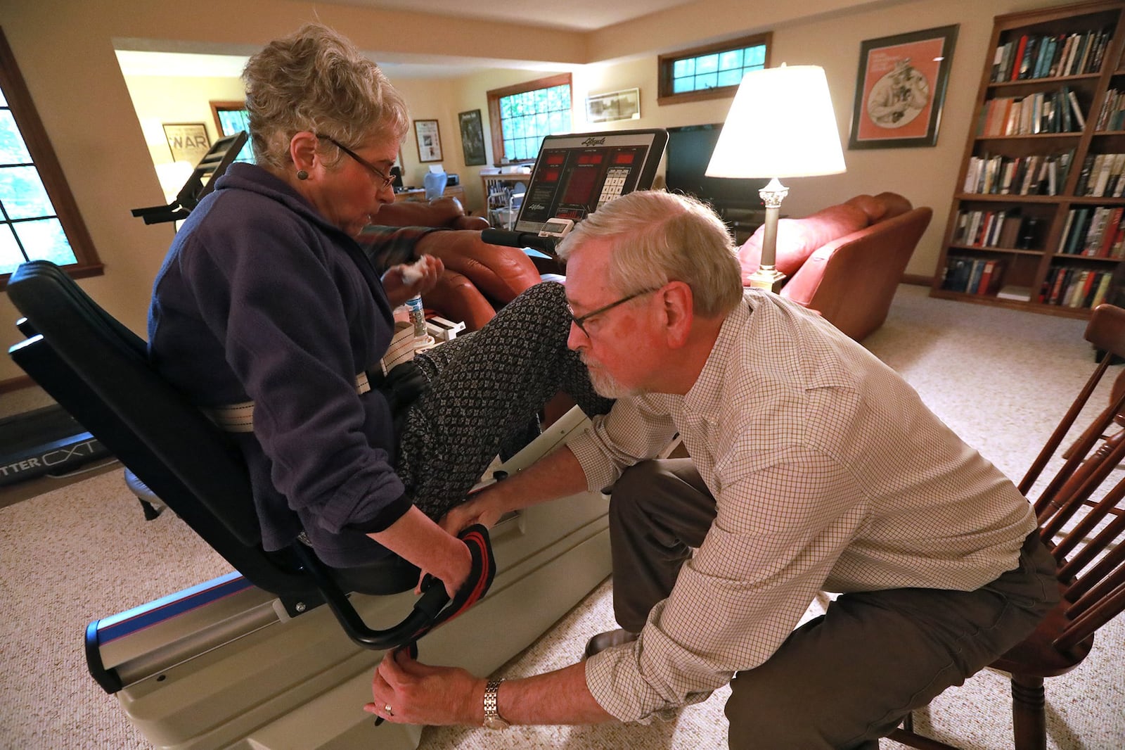 Steve Sidlo helps his wife, Cynthia, get into position on her exercise bike Wednesday in their Springfield home. Cynthia is recovering from a stroke several years ago. BILL LACKEY/STAFF