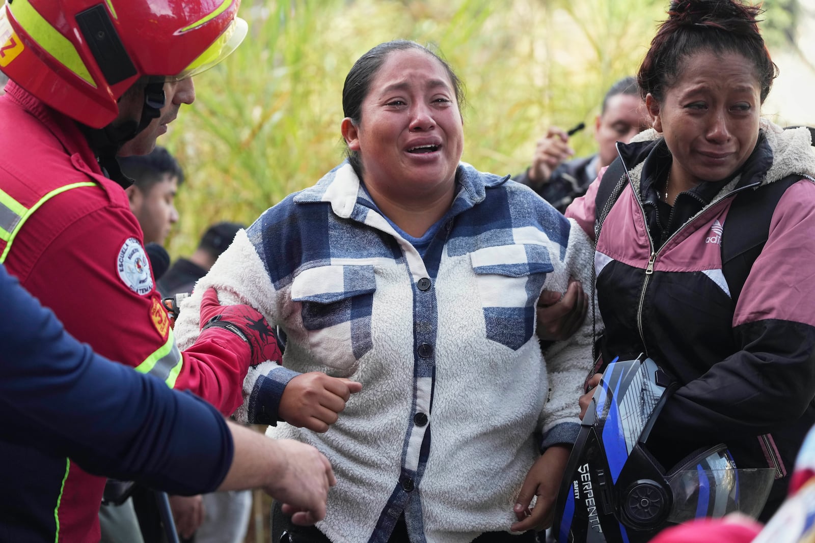 Women stand at the scene of a crash, uncertain if their loved ones were among the passengers of a bus that fell from a bridge, on the outskirts of Guatemala City, Monday, Feb. 10, 2025. (AP Photo/Moises Castillo)