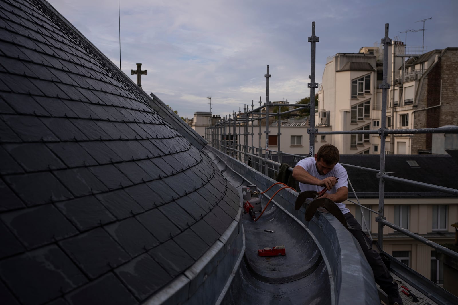 A roofer solders on the zinc gutter of a church in Paris, Tuesday, Oct. 15, 2024. (AP Photo/Louise Delmotte)