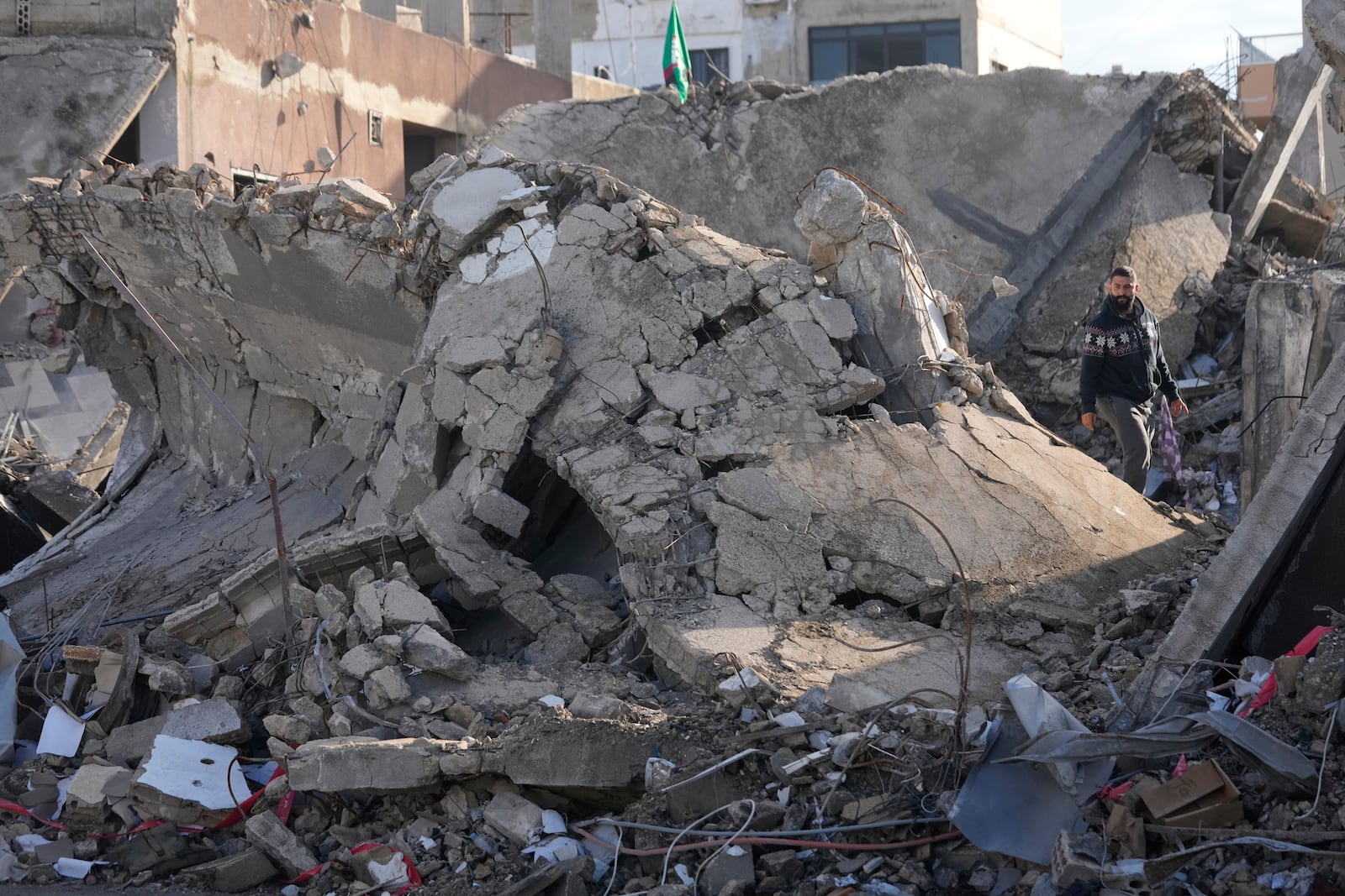 A man stands on the rubble of a destroyed building that housed his apartment in Tyre, southern Lebanon, Thursday, Nov. 28, 2024. (AP Photo/Hussein Malla)