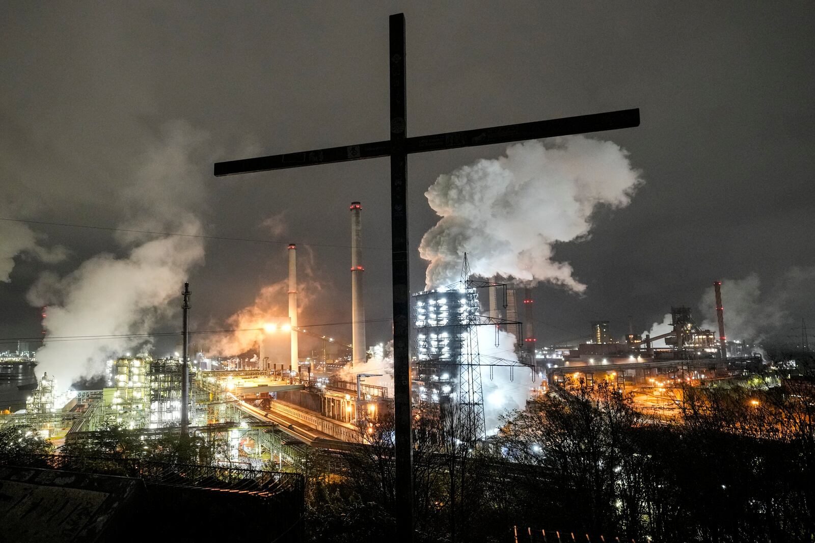 FILE - A cross can be seen in front of the steaming Schwelgern coking plant of German troubled steel producer thyssenkrupp in Duisburg, Germany, Thursday, Nov. 14, 2024. (AP Photo/Martin Meissner, File)