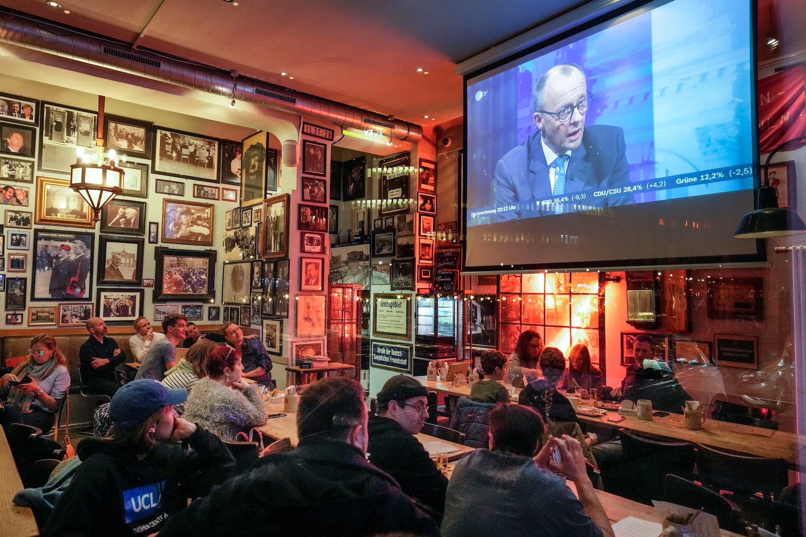 People watch a tv discussion with Friedrich Merz, leader of the German Christian Democratic Union (CDU), at a pub in Berlin, Germany, Sunday, Feb. 23, 2025, after the German national election. (AP Photo/Martin Meissner)