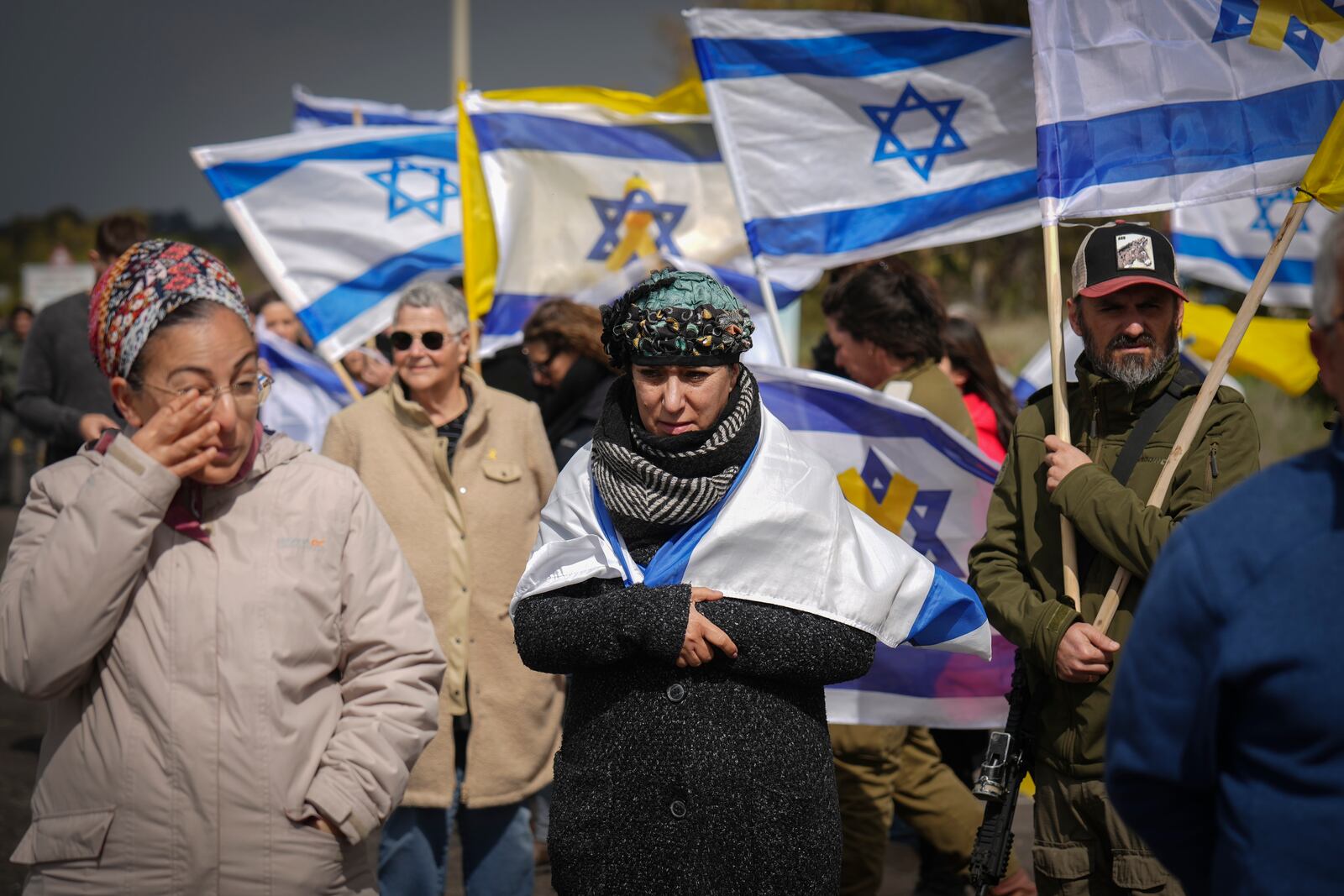 Israelis hold flags as they watch a convoy carrying the coffins containing the bodies of four Israeli hostages, including a mother and her two children just handed over by Palestinian militant groups in Gaza, drives by a road near Kibbutz Reim, southern Israel, Thursday, Feb. 20, 2025.(AP Photo/Ariel Schalit)