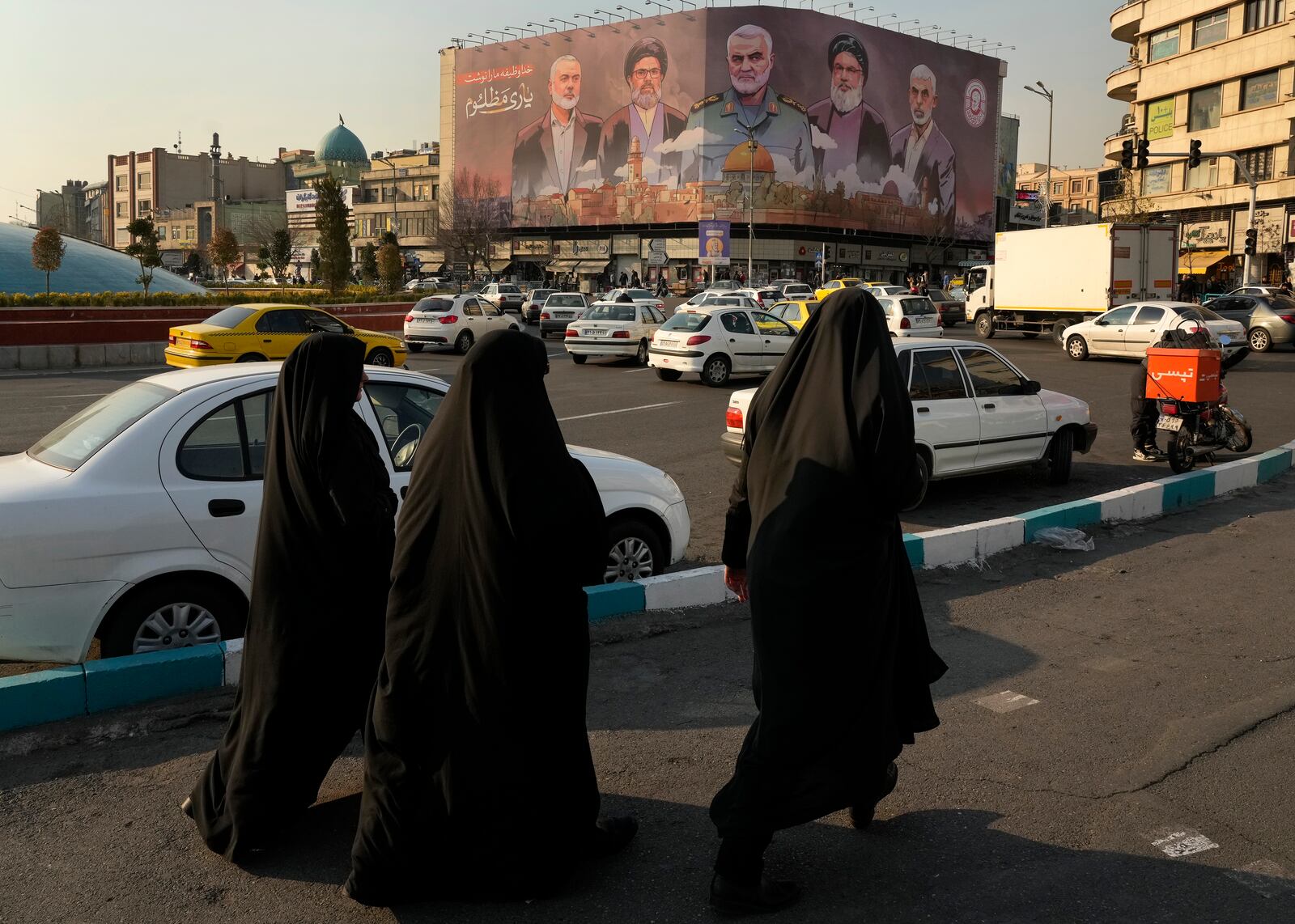 People walk on Enqelab-e-Eslami (Islamic Revolution) square near a huge banner showing the late commander of the Iran's Revolutionary Guard expeditionary Quds Force, Gen. Qassem Soleimani, center, who was killed in a U.S. drone attack in 2020, and Hezbollah and Hamas officials killed by Israel, in Tehran, Iran, Tuesday, Jan. 21, 2025. (AP Photo/Vahid Salemi)