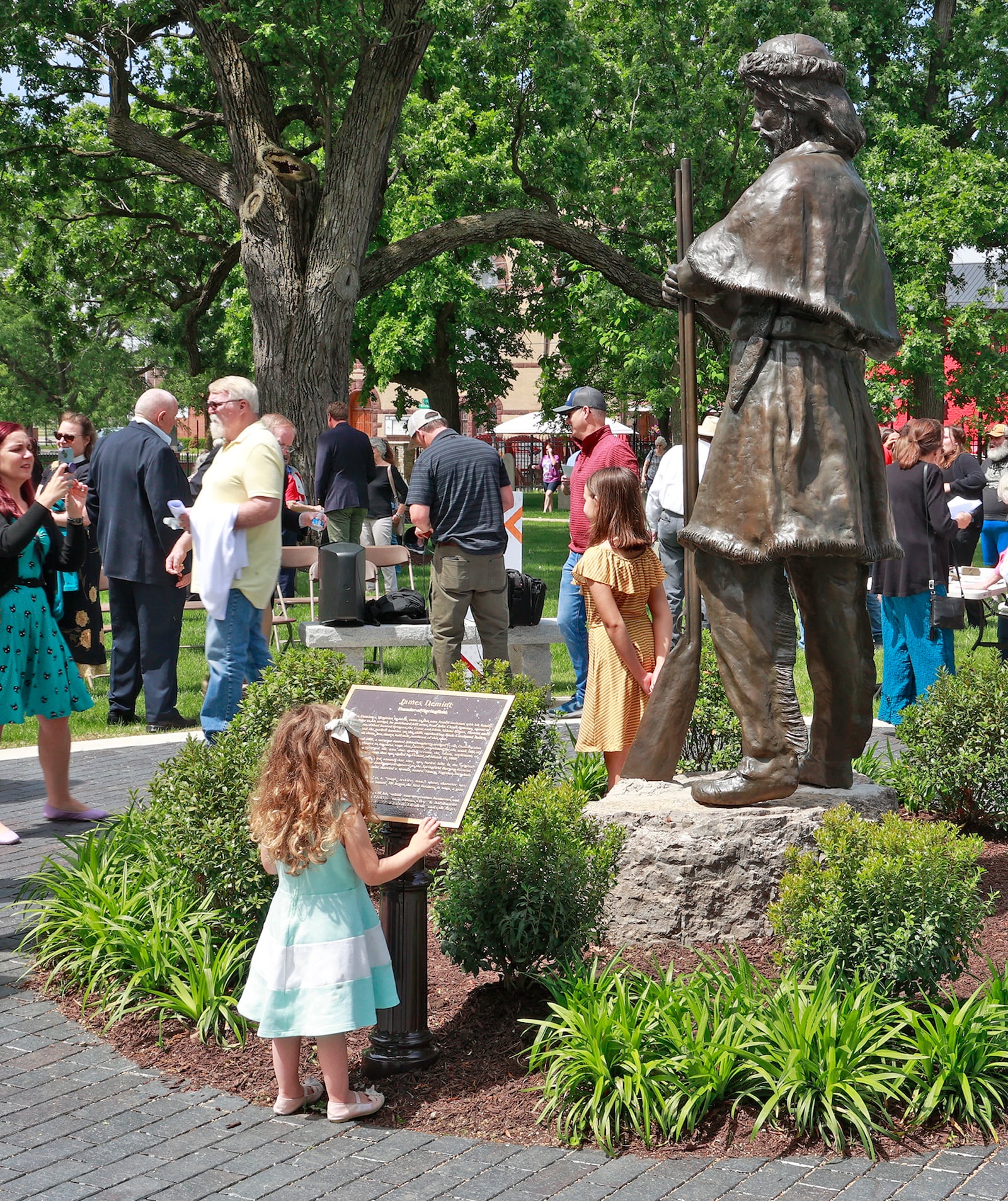 Violet Shumaker looks over the plaque that accompanies the statue her ancestor, Springfield founder James Demint, during  dedication ceremonySaturday, May 27, 2023 for the renovated Springfield Burying Ground in downtown Springfield. The Burying Ground, opened in 1801, recently underwent a $1.2 million renovation. Several Revolutionary War veterans are buried in cemetery along with the founding fathers of Springfield. New grave markers have been added along with historic plaques and a statue of Springfield founder James Demint. BILL LACKEY/STAFF