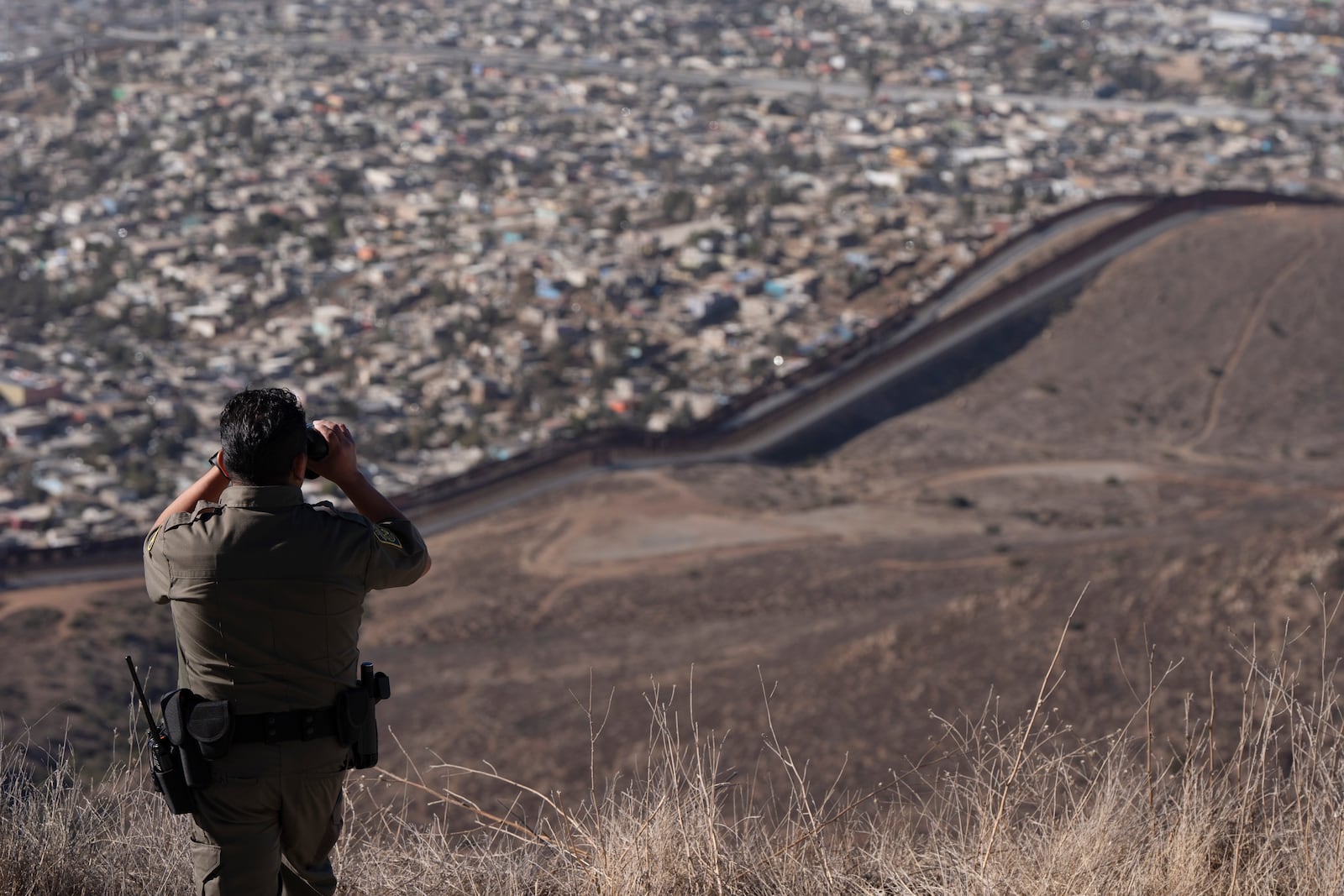 Border Patrol Agent Gutierrez looks through binoculars towards two border walls separating Mexico from the United States, Thursday, Jan. 23, 2025, in San Diego. (AP Photo/Gregory Bull)