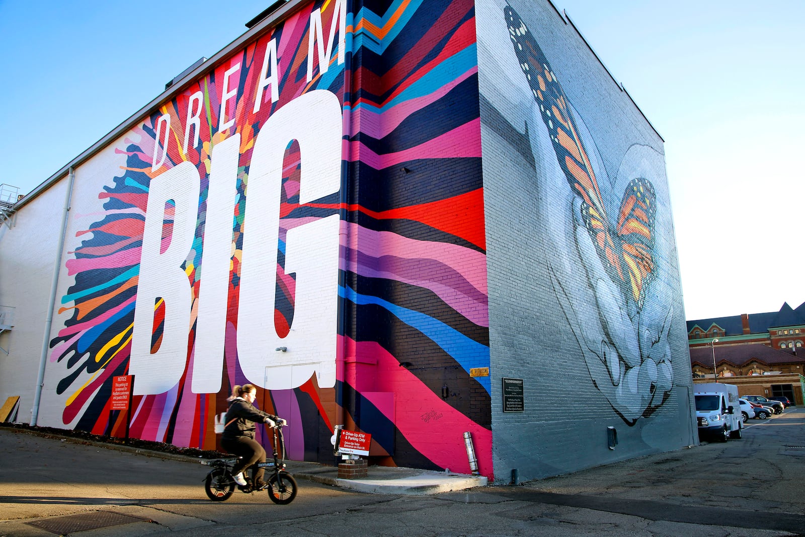 Kaylie Craig rides her electric bike past the newest mural in the downtown Springfield area. The "DREAM BIG" mural on the north side of the State Theater was created by artist Jeremy Jarvis and has 75 different colors in it. The new mural joins the "Transformation" mural on the west side of the theater. BILL LACKEY/STAFF