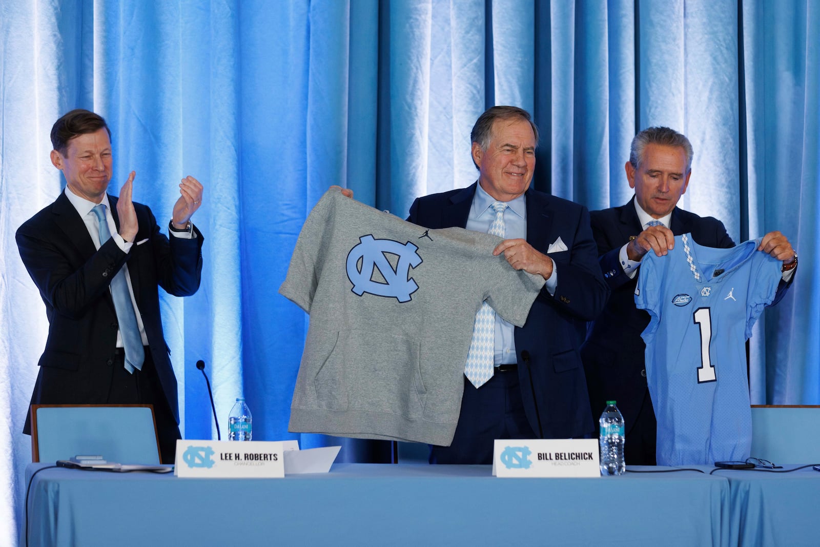 New North Carolina head football coach Bill Belichick, center, holds up a UNC branded sleeveless hoodie between North Carolina Chancellor Lee Roberts, left, and athletic director Bubba Cunningham, right, during an NCAA college football press conference in Chapel Hill, N.C., Thursday, Dec. 12, 2024. (AP Photo/Ben McKeown)