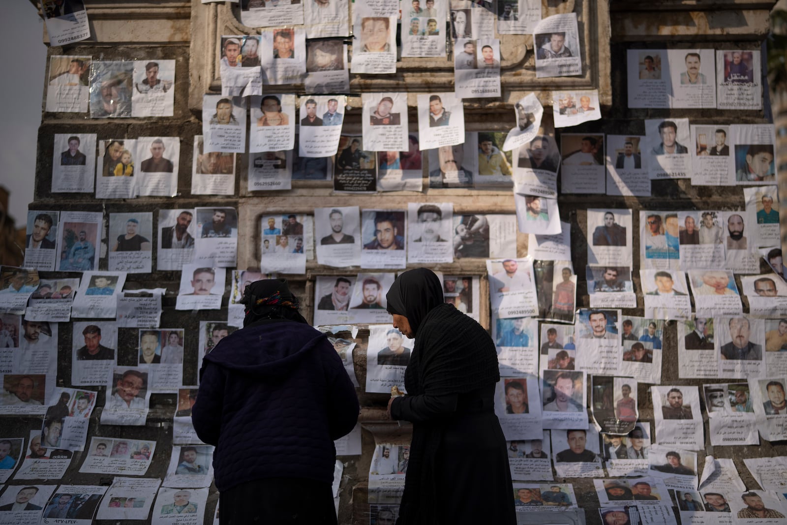 Women look at photos of people reported to be missing by members of ousted Syrian President Bashar Assad's army, or a pro-government militia, in the Marjeh square in Damascus, Syria, Sunday, Dec. 22, 2024. (AP Photo/Leo Correa)