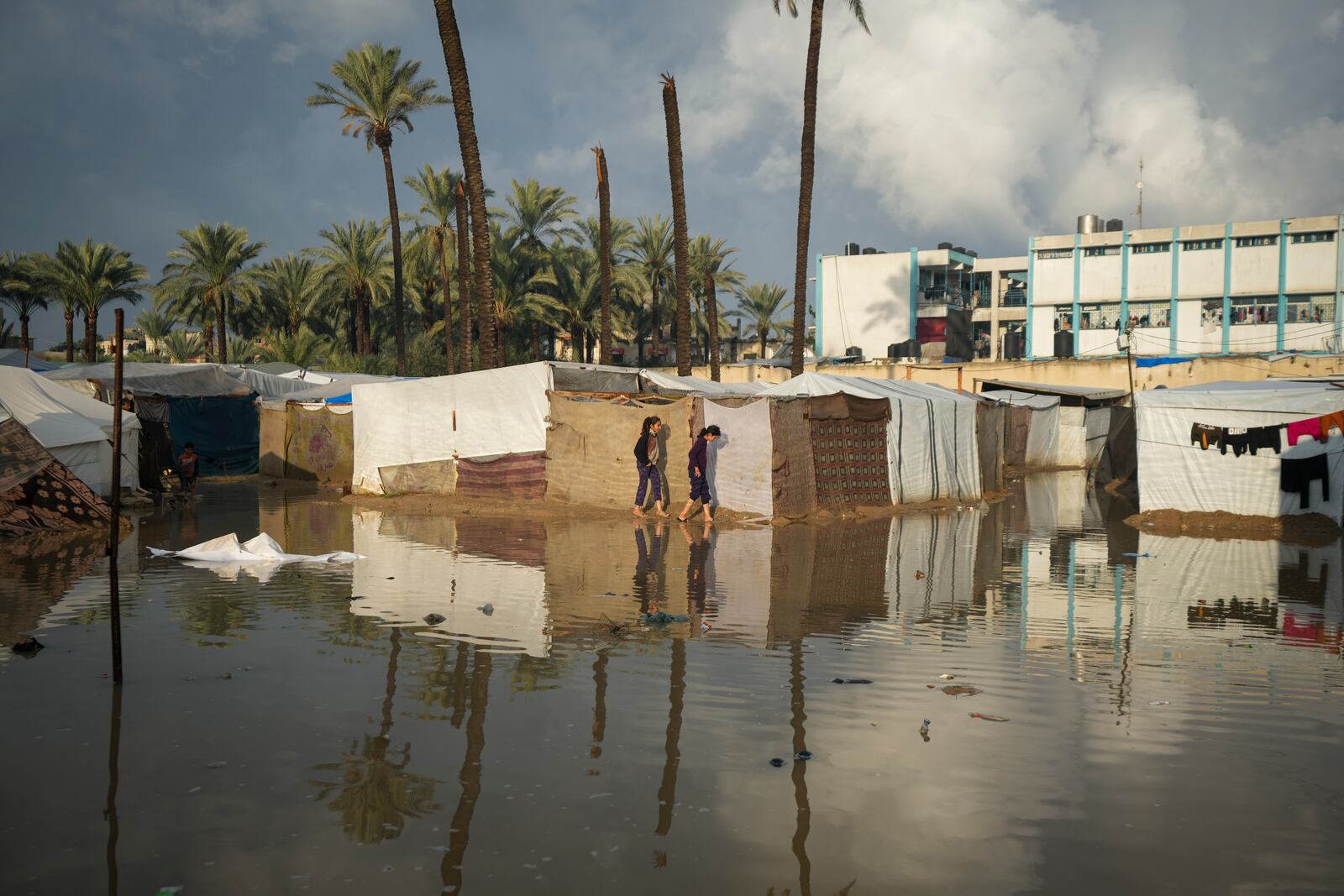 Two Palestinian girls attempt to walk through a flooded area after a night of heavy rainfall at a tent camp for displaced Palestinians in Deir al-Balah, central Gaza Strip, Thursday January. 23, 2025. (AP Photo/Abdel Kareem Hana)