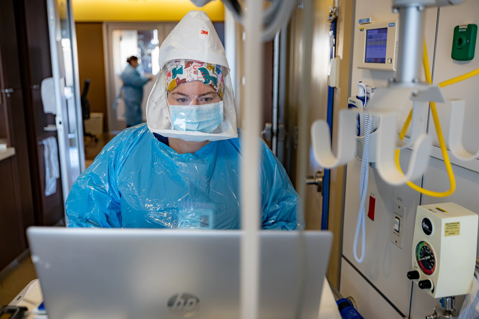 Taylor Spicer is a nurse at Miami Valley Hospital nurse. She is wearing full personal protective equipment, including an oxygen tank on her back, as she enters data for a COVID-19 patient in the hospital's COVID-19 unit.