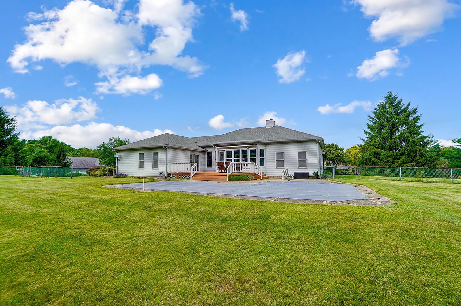 The rear of the home has a wood deck with railings, a retractable awning, concrete patio and in ground pool. There is also a chain link fence.