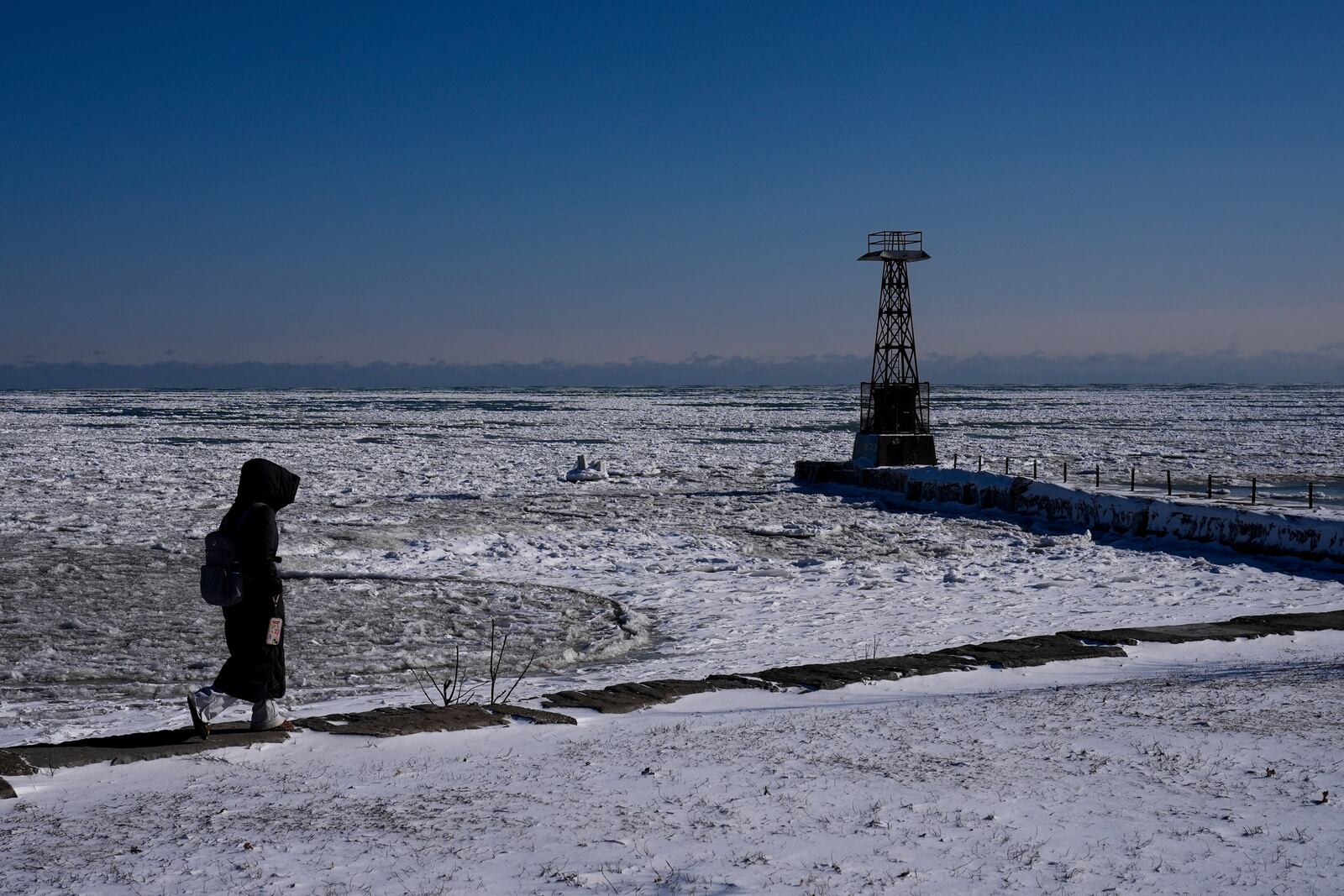 A person walks along the shore of ice covered Lake Michigan Thursday, Feb. 13, 2025, in Chicago. (AP Photo/Kiichiro Sato)