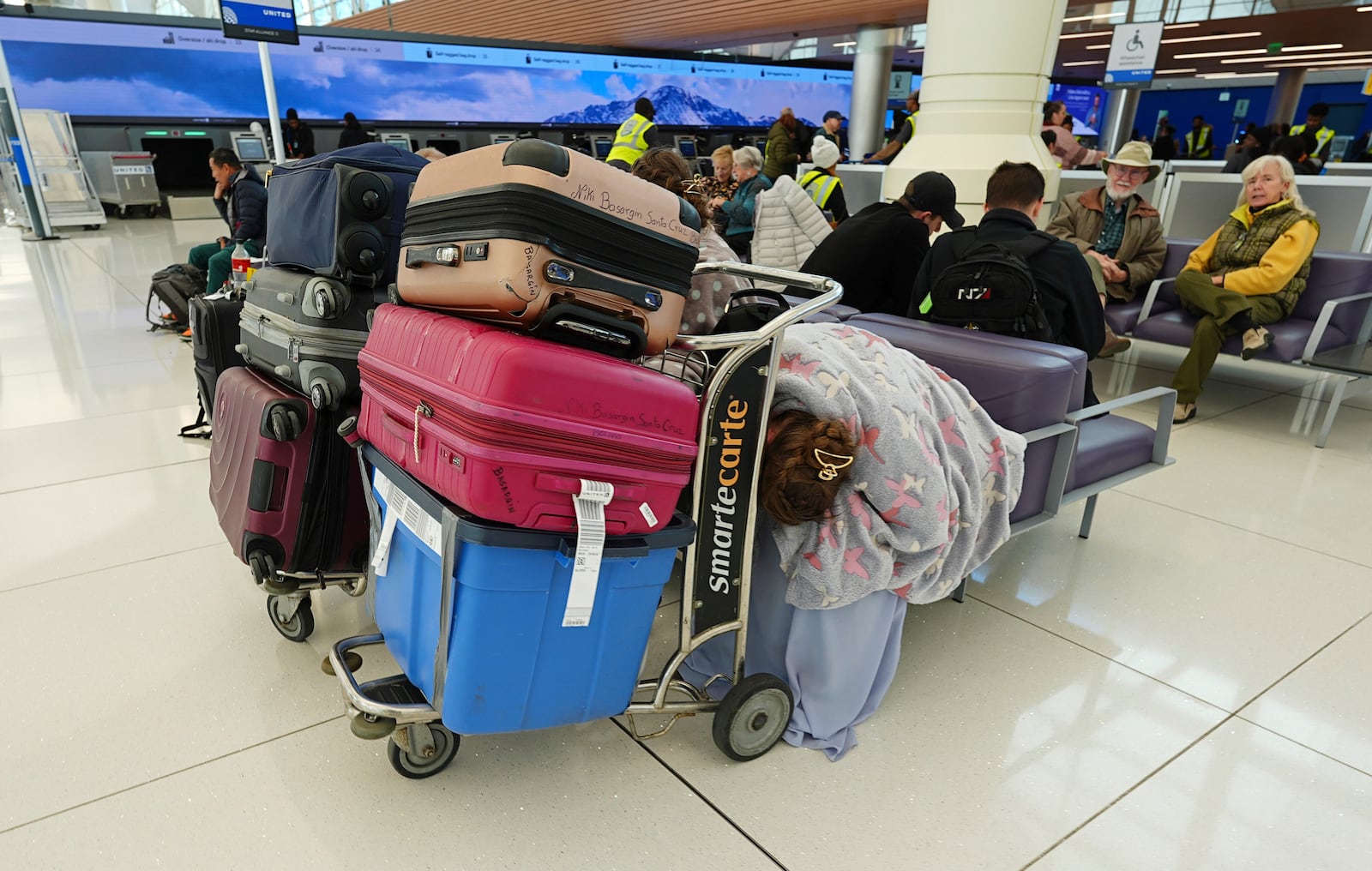 A traveler sleeps by carts of her belongings near the Southwest Airlines counter in Denver International Airport Tuesday, Nov. 26, 2024, in Denver. (AP Photo/David Zalubowski)