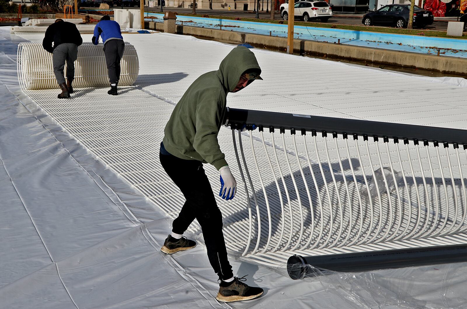 A crew from All Year Sports Galaxy works to build a temporary ice skating rink on the Springfield City Hall Plaza Thursday. The workers unrolled sheets of plastic tubing that will cool the water from underneath. The Greater Springfield Partnership will open the skating rink on Nov. 26 at 5 p.m. prior to the city’s Grand Illumination event. The ice rink, which is 40 feet by 80 feet, will be open on Thursdays through Sundays until Jan. 2. The cost to use the ice rink will be $5, including skate rental.. BILL LACKEY/STAFF